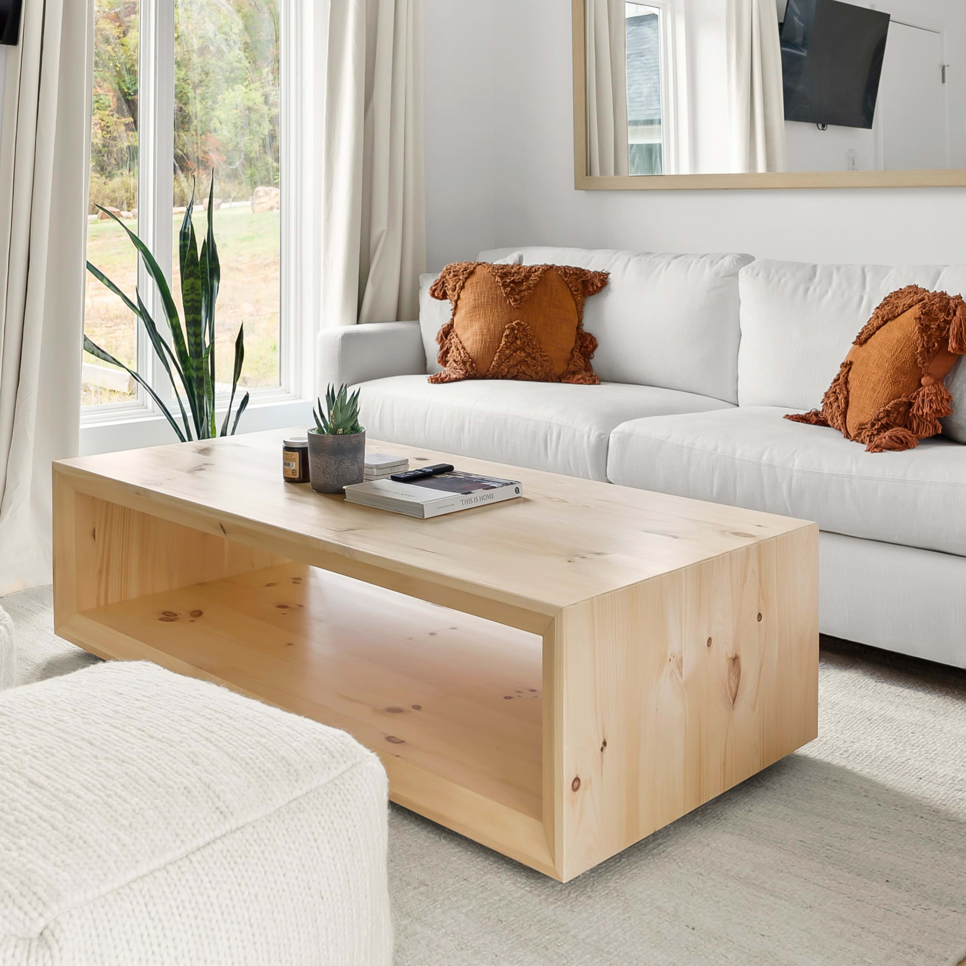 A modern living room with a white sofa adorned with orange cushions, a wooden coffee table, and two round, textured ottomans.