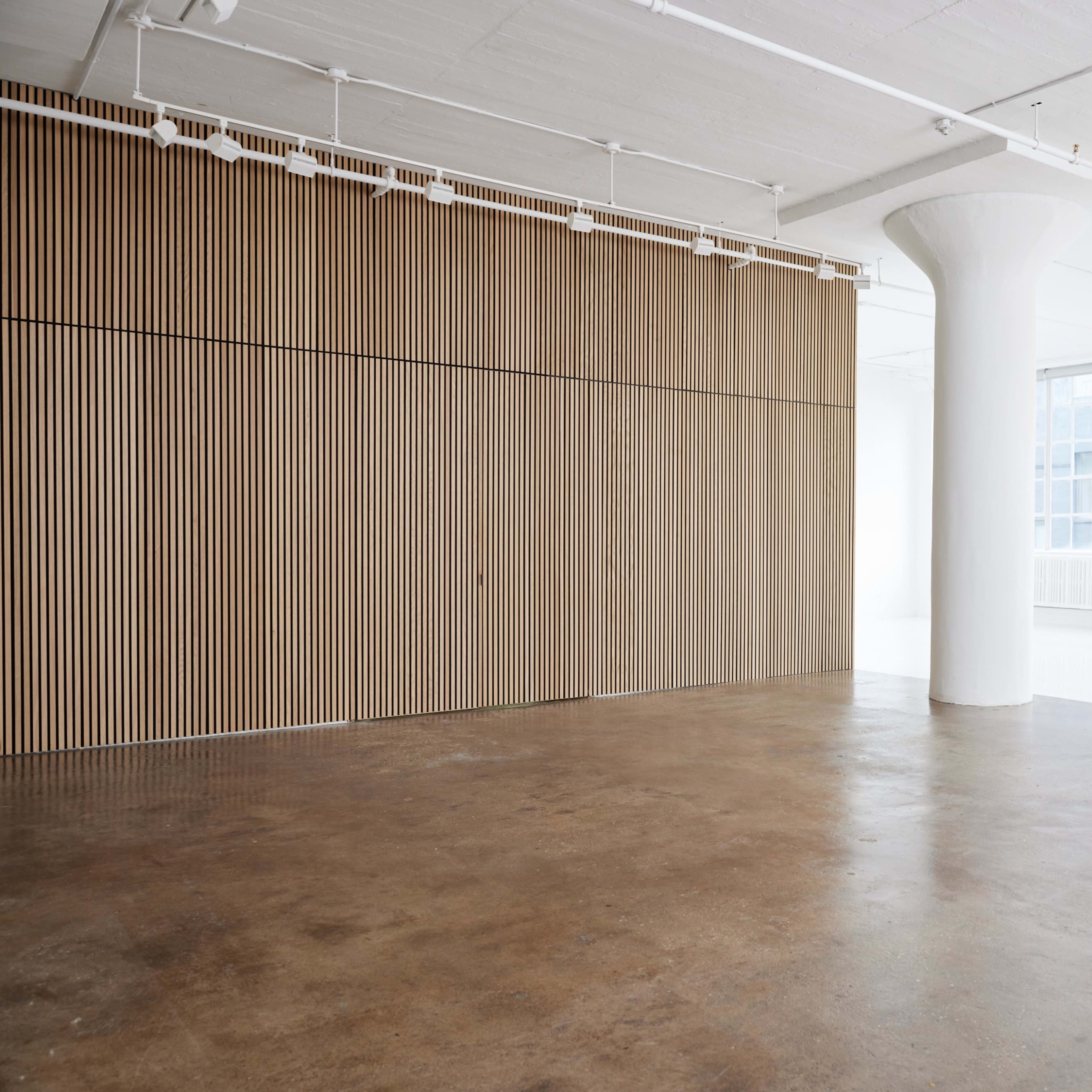 A spacious, minimalist interior with wooden paneling on one wall and large windows allowing natural light to fill the room.