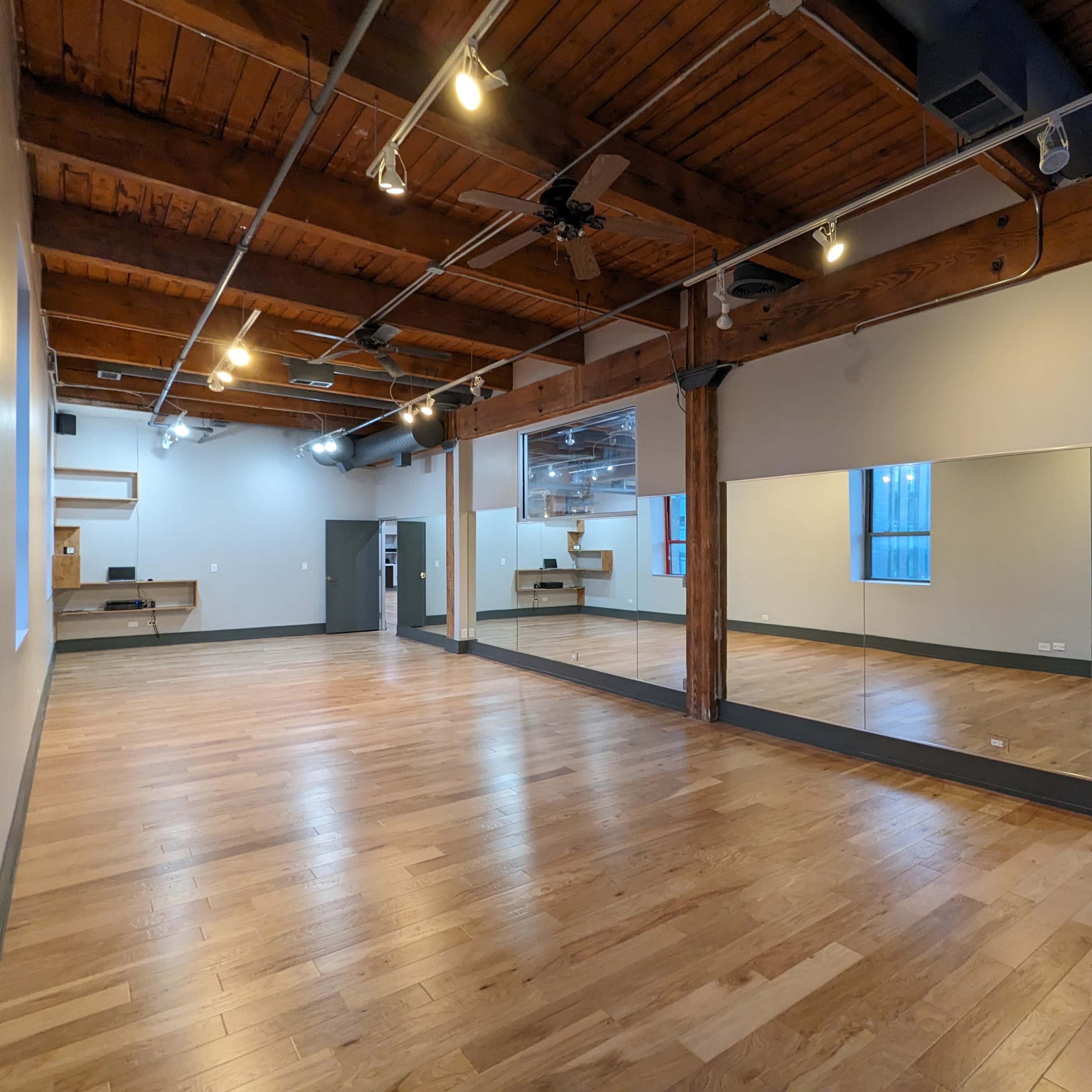 A spacious studio with wooden floors, exposed beams, and a large mirror along one wall.