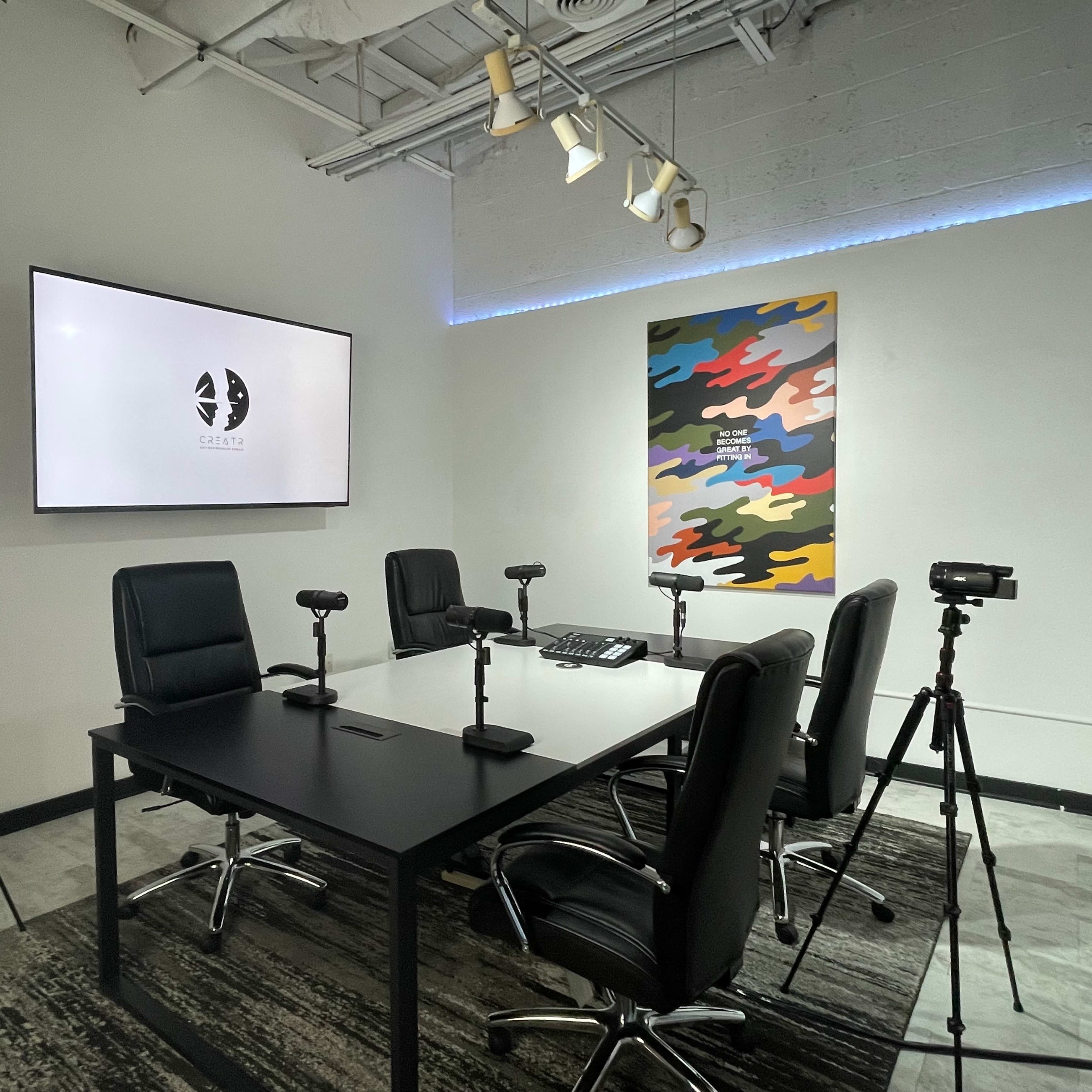 A modern conference room features a large display screen, a central table with chairs, and several cameras positioned on tripods.