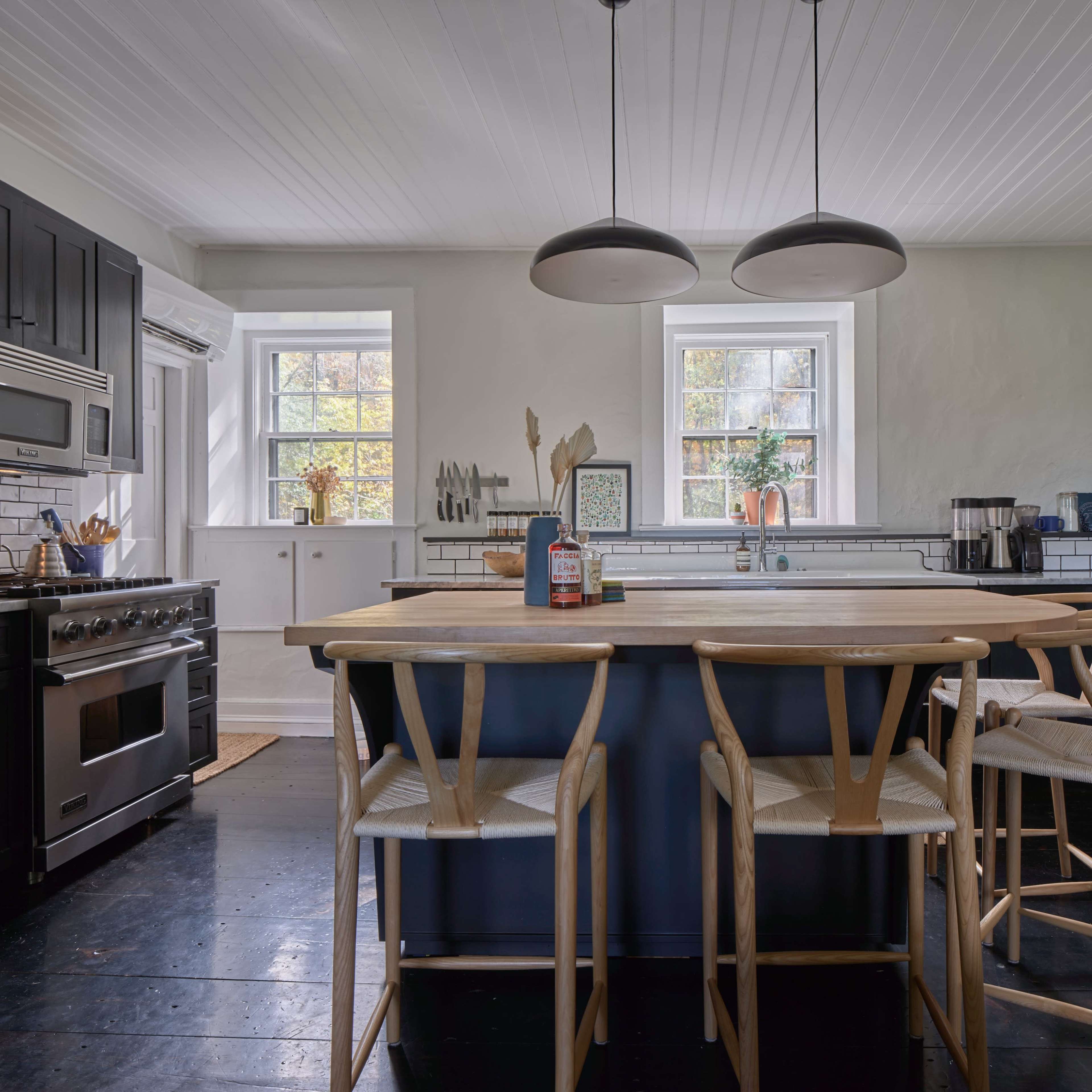 The kitchen features a central island with wooden bar stools, a gas range, and large windows letting in natural light.