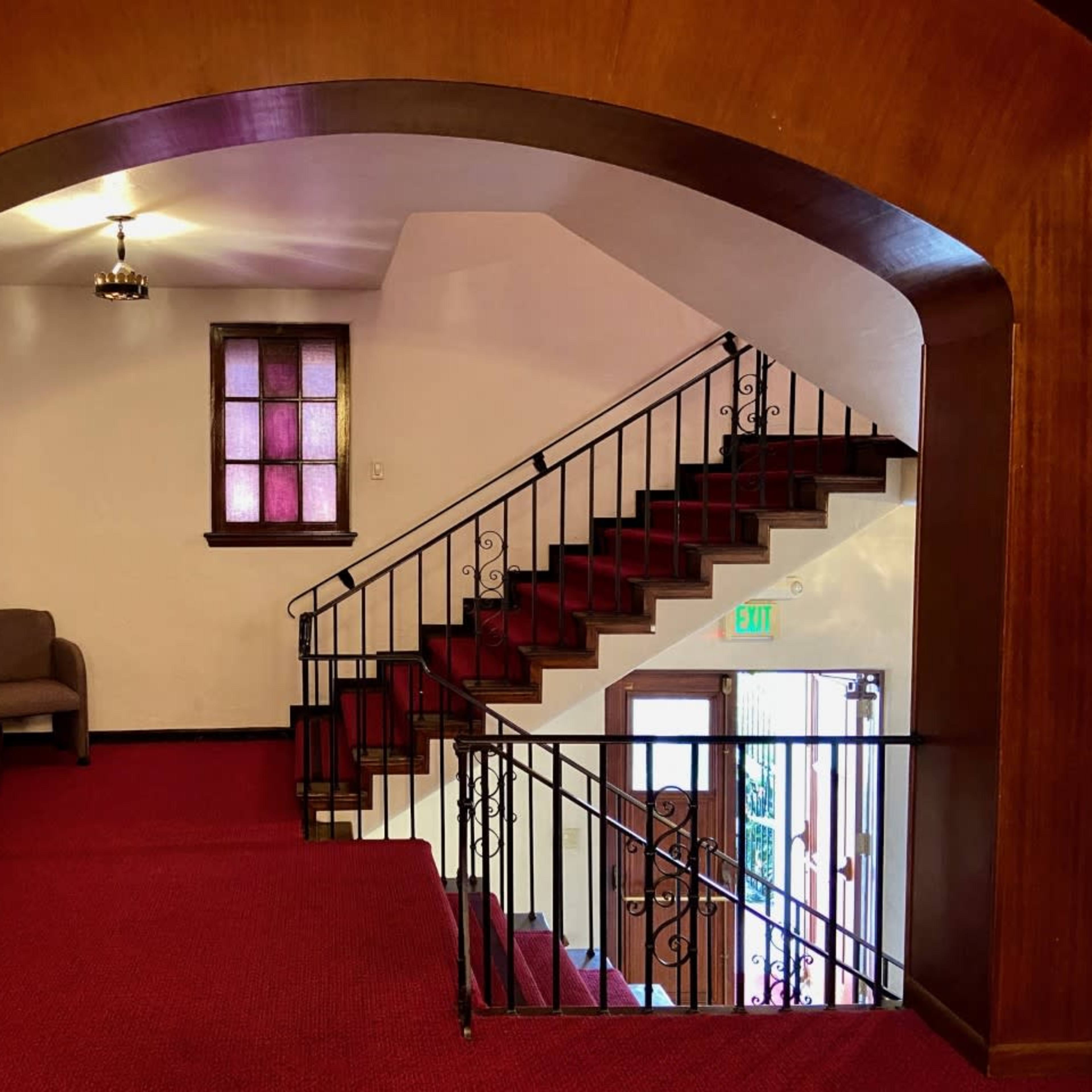 A staircase with a wooden archway leading to a landing area featuring two chairs and a window with patterned glass.