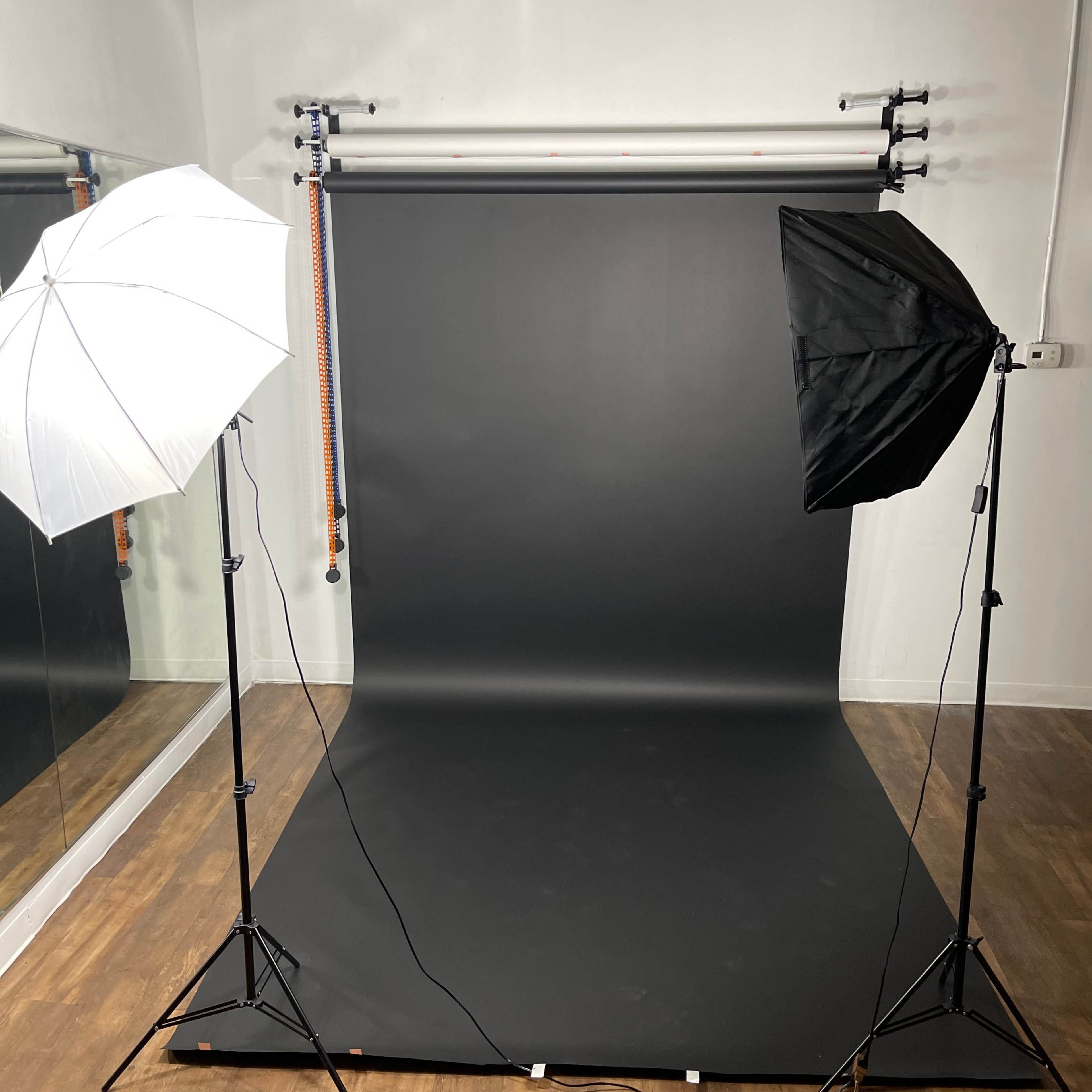 A photography studio with a black backdrop, two light umbrellas on tripods, and a mirrored wall.