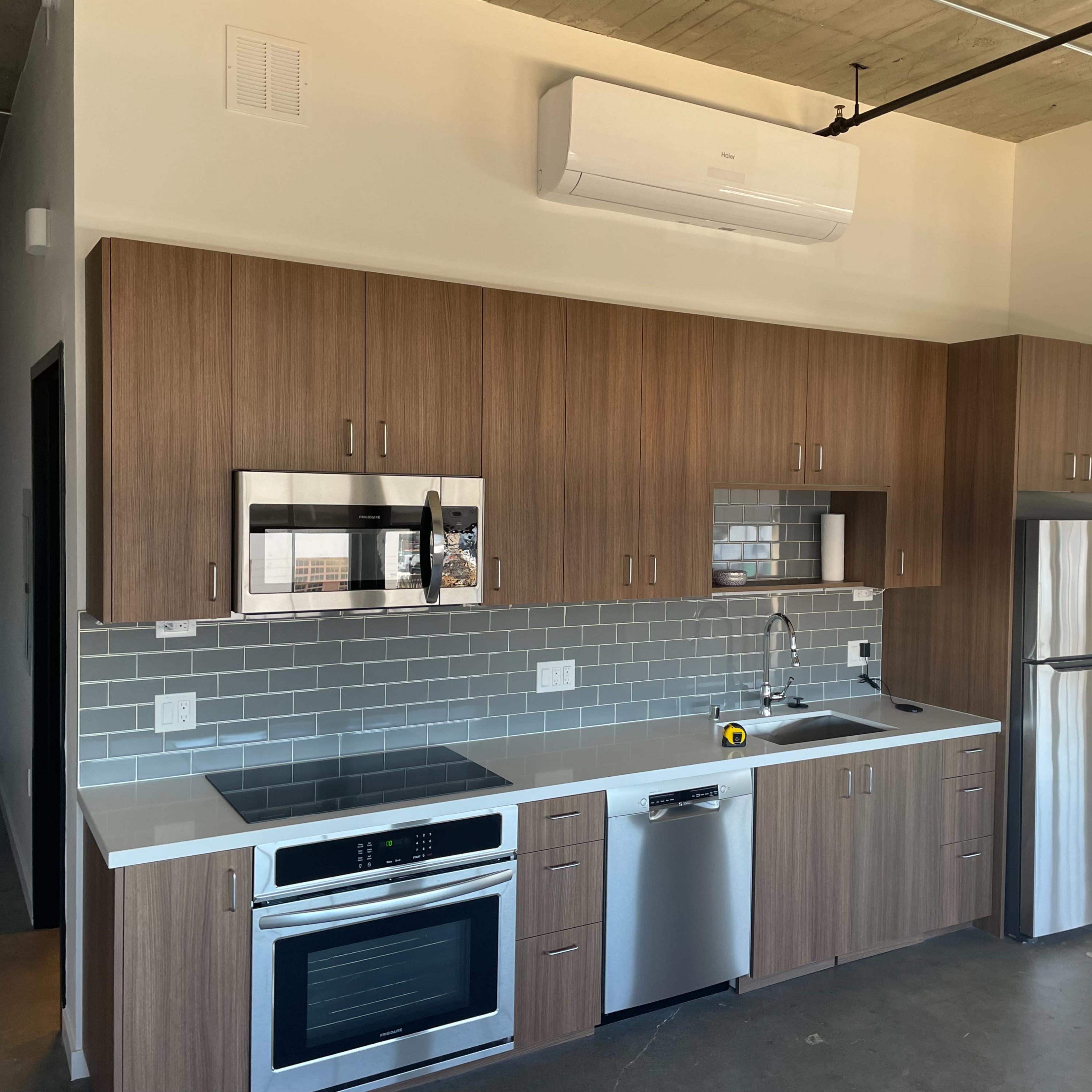 A modern kitchen featuring wooden cabinets, stainless steel appliances, and gray tile backsplash.