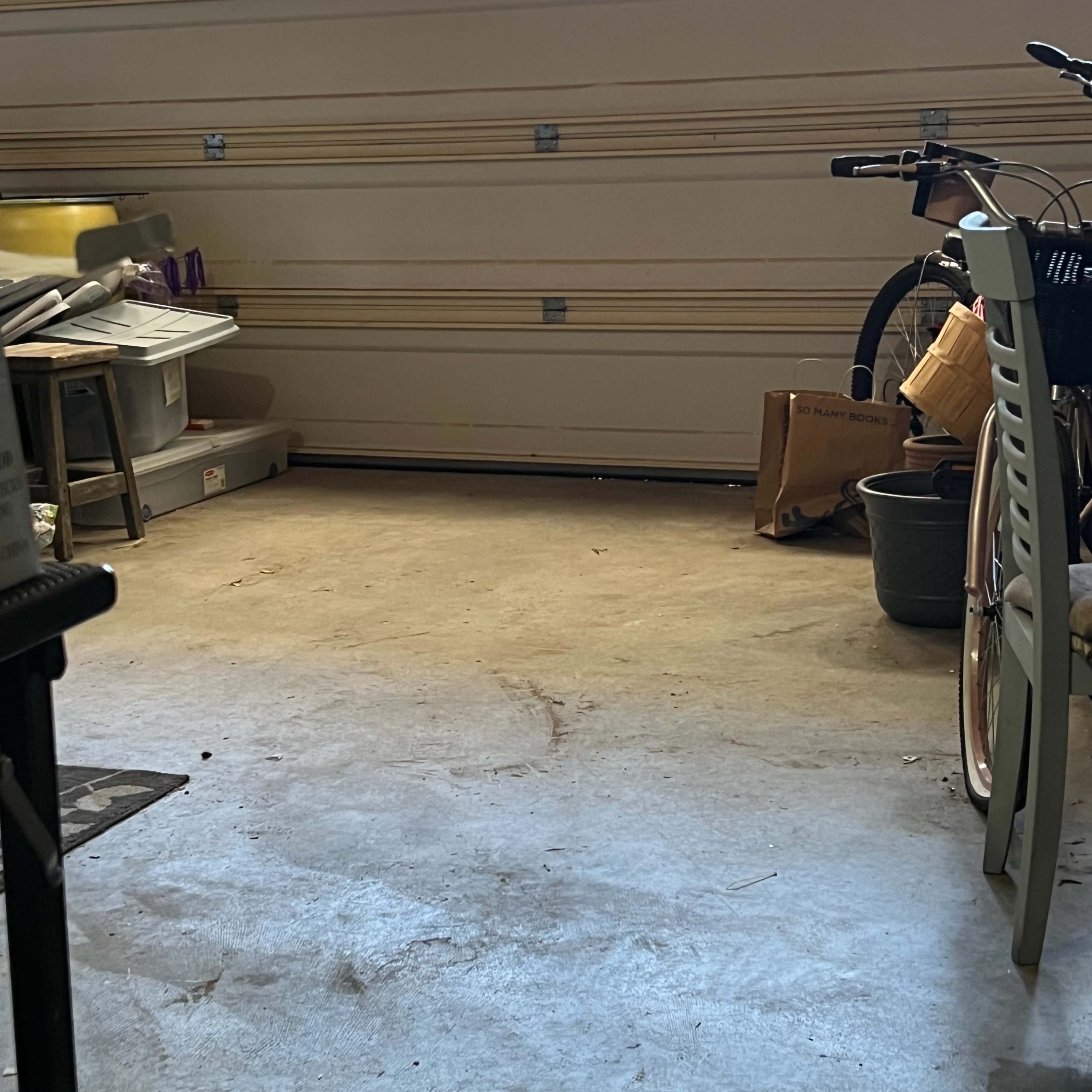 A garage with a concrete floor, storage bins, a bicycle, and a partially open garage door allowing natural light to enter.