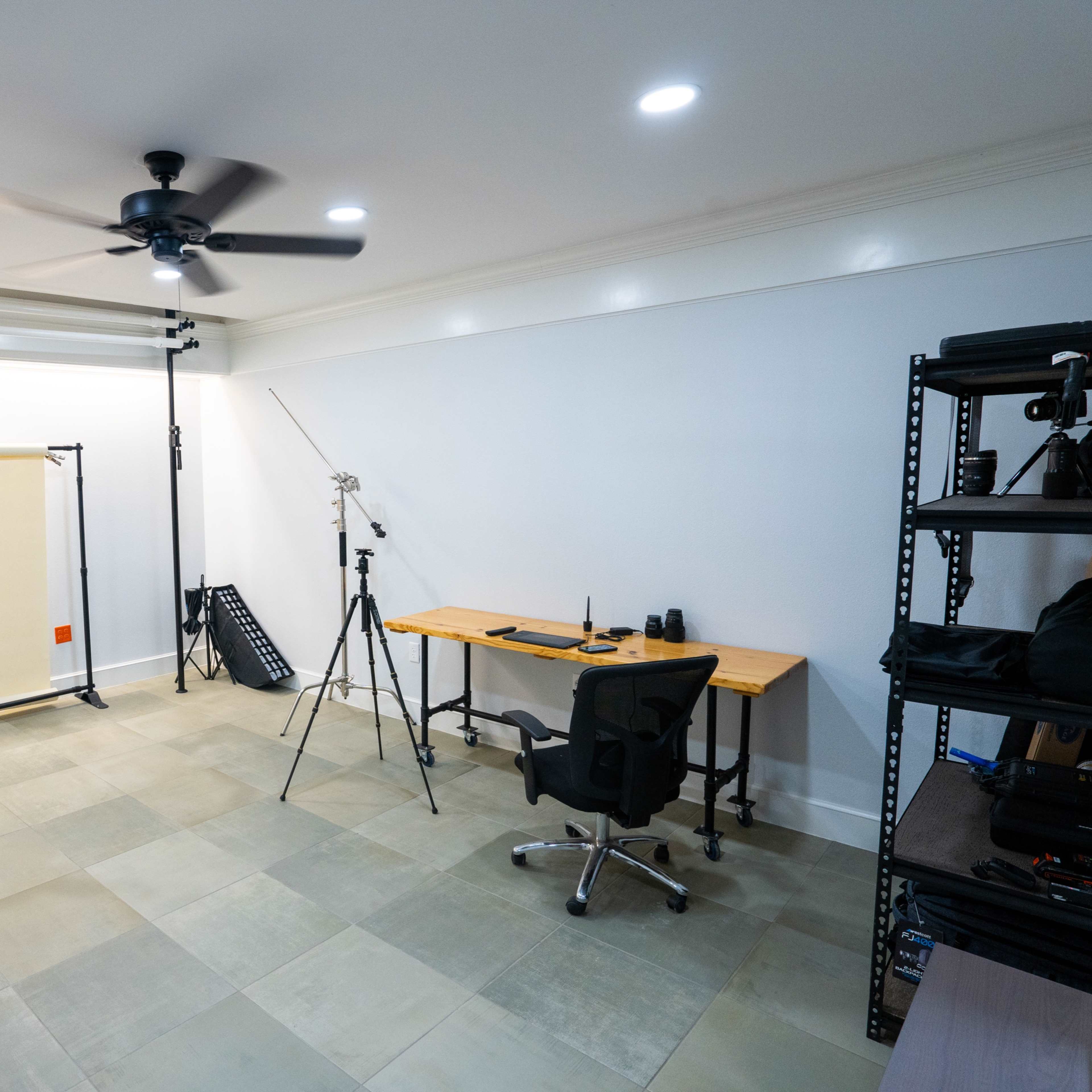 A photography studio setup with a backdrop, lighting equipment, a desk, and a chair on a tiled floor.