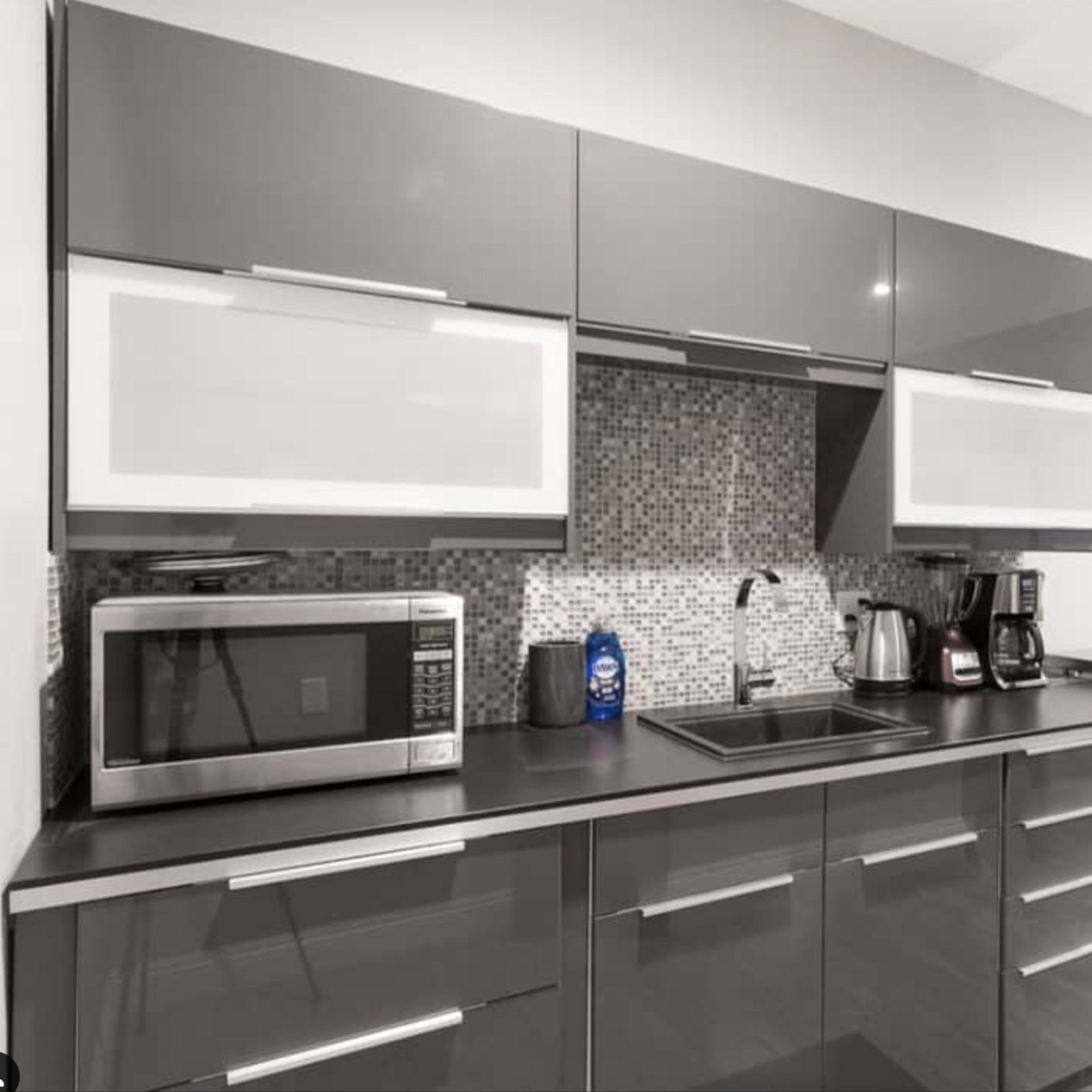 A modern kitchen with dark cabinetry, a stainless steel microwave, a coffee maker, and a small table on the side.