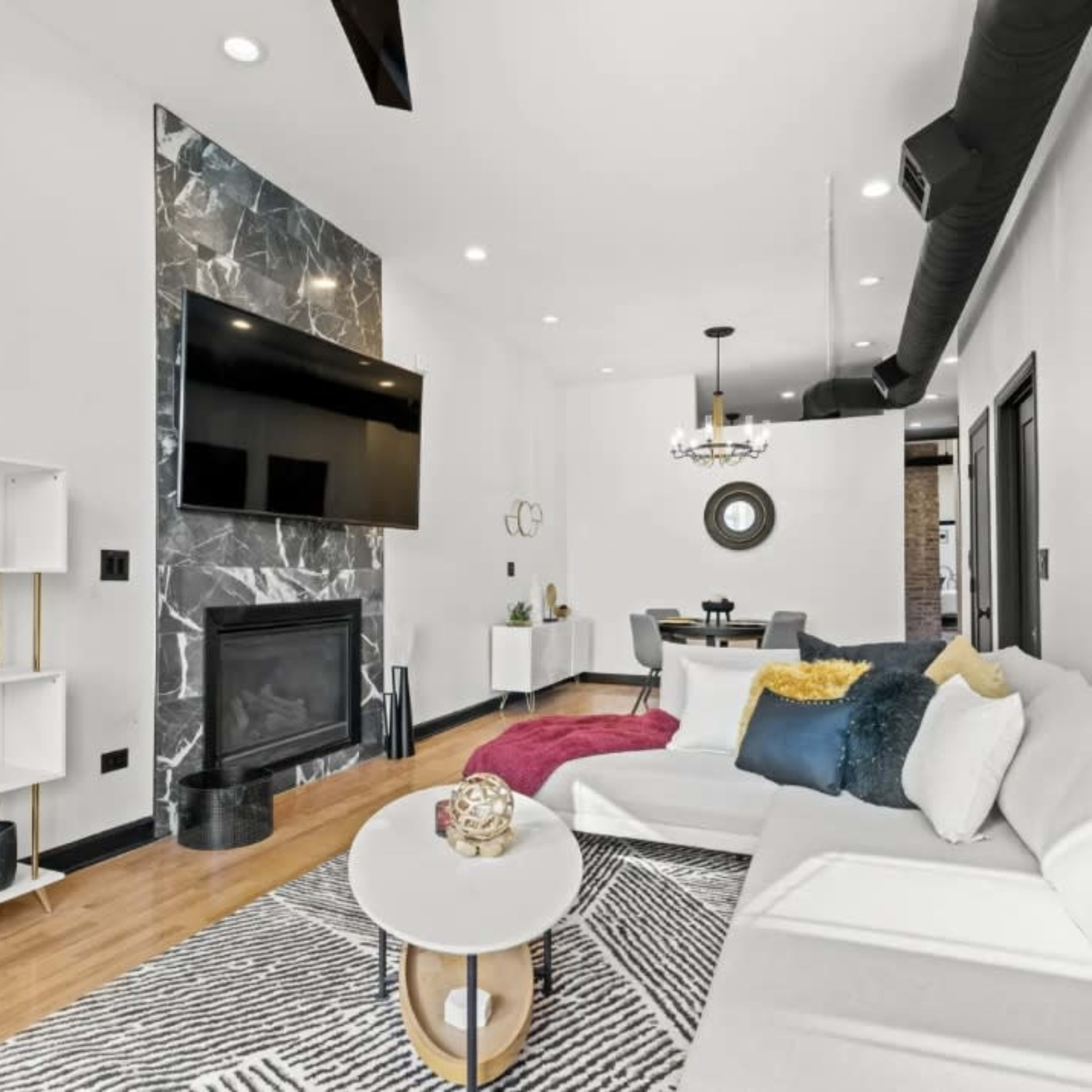 A modern living room features a sleek sofa, a marble fireplace, and a large wall-mounted television.
