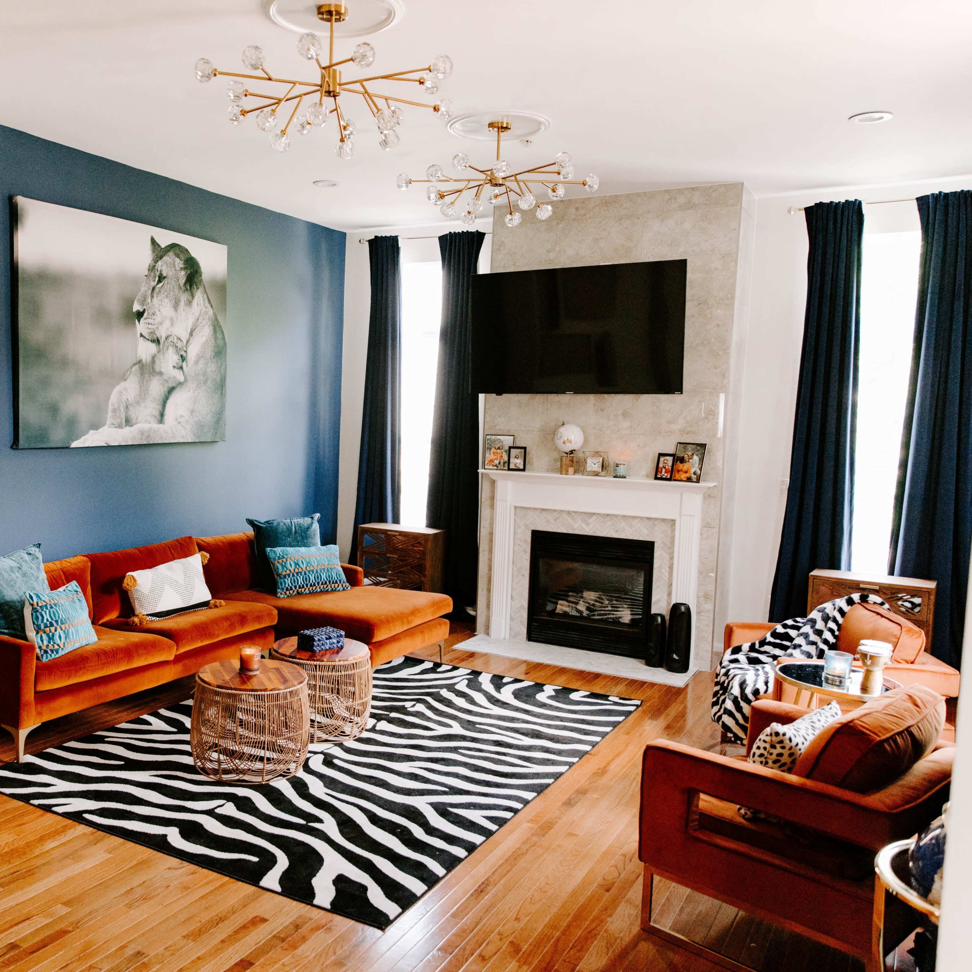 The living room features a blue accent wall, a stone fireplace, two sets of seating, and a zebra-patterned rug.
