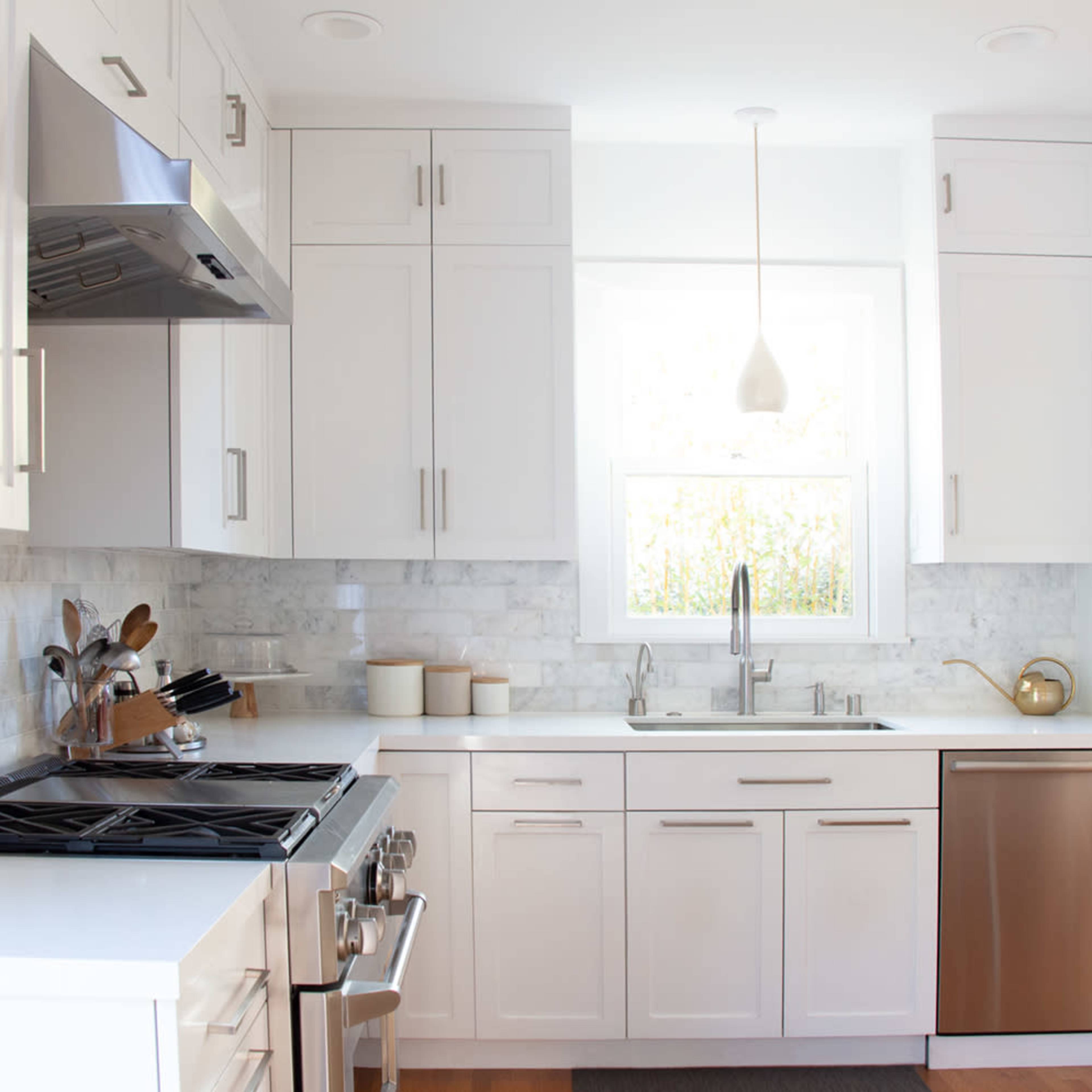 A modern kitchen features white cabinets, a stainless steel oven, a sink with a polished faucet, and a window above the sink.