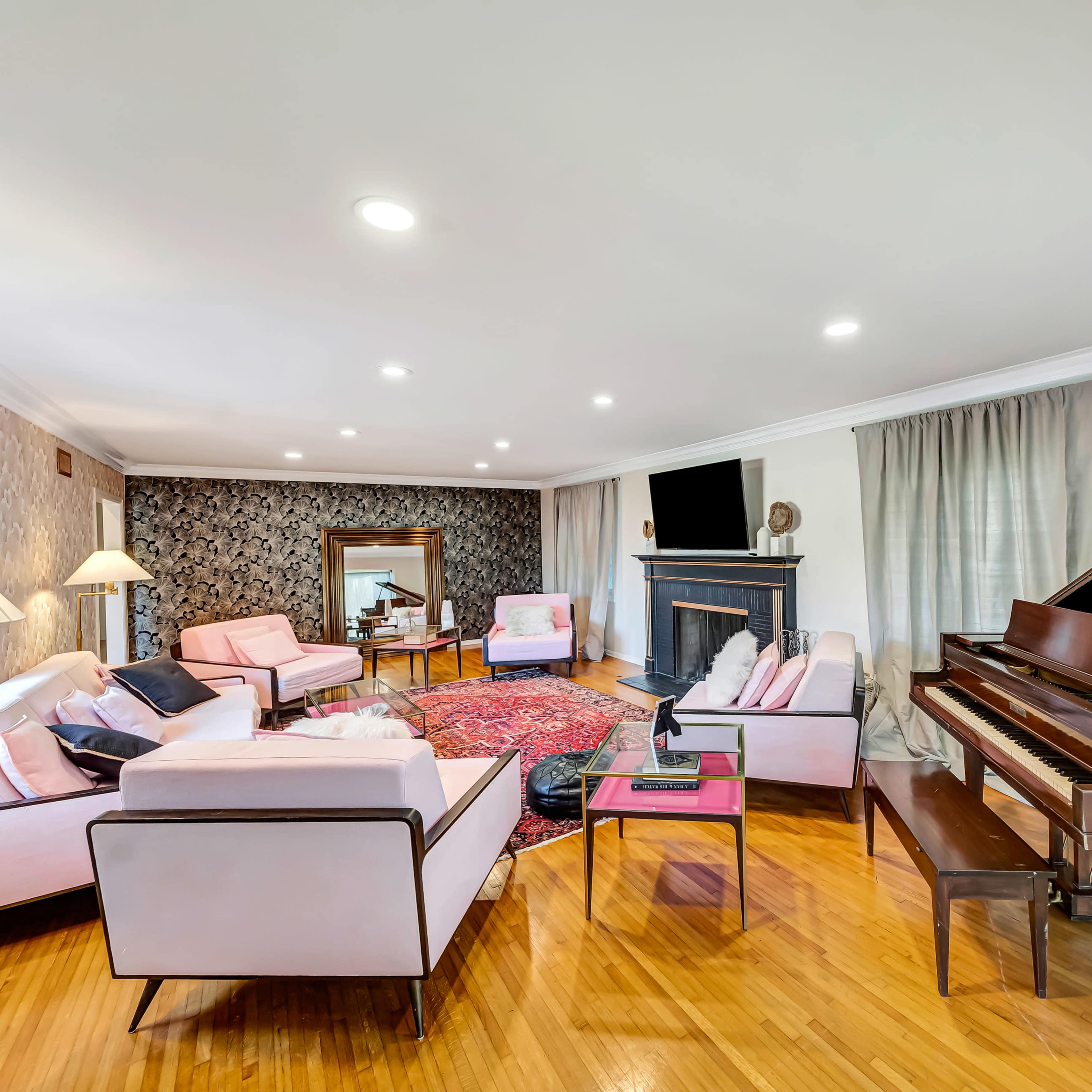 A modern living room featuring a grand piano, pink upholstered furniture, a large area rug, and a fireplace.