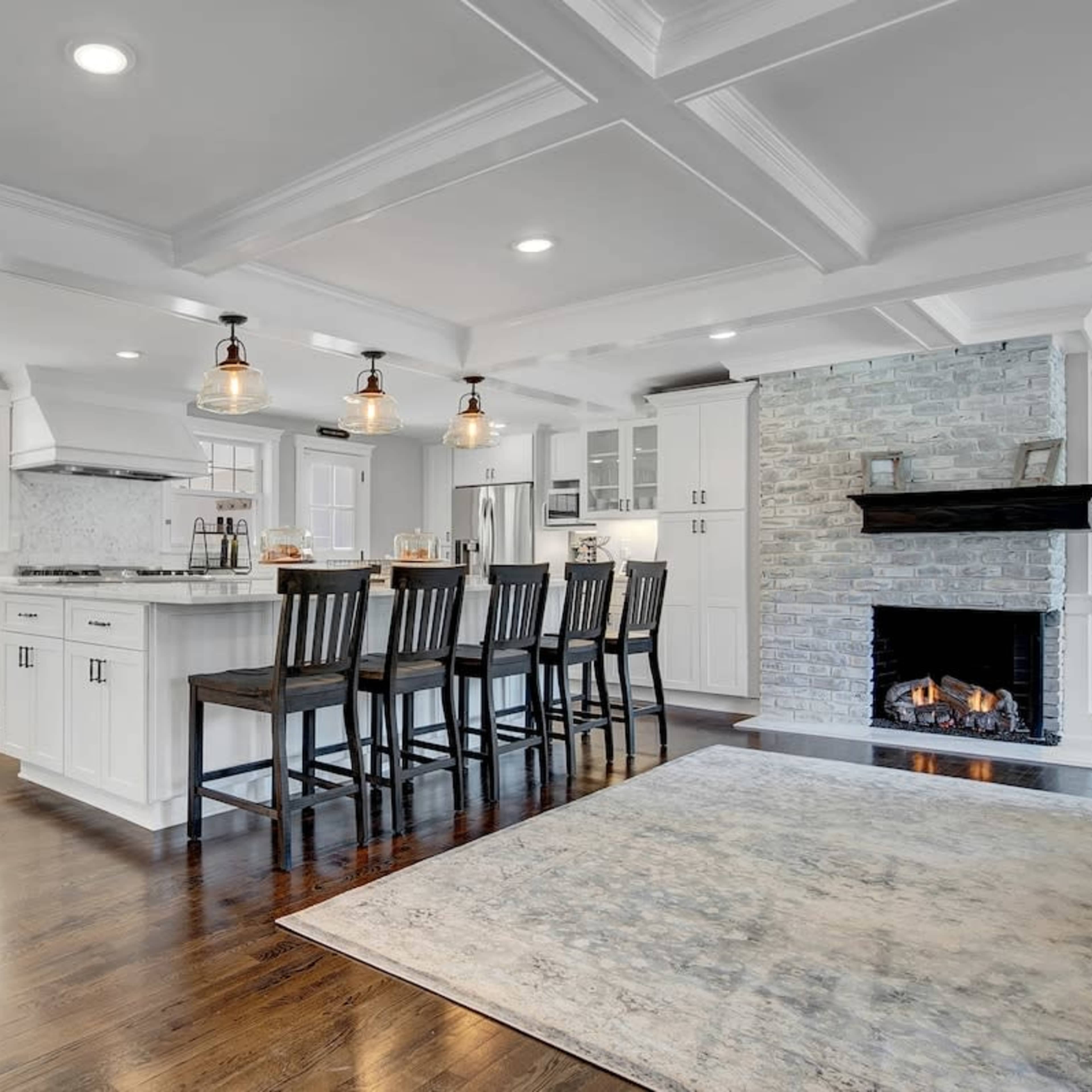 A modern kitchen with white cabinetry, a large island with seating, and a stone fireplace in a spacious layout.