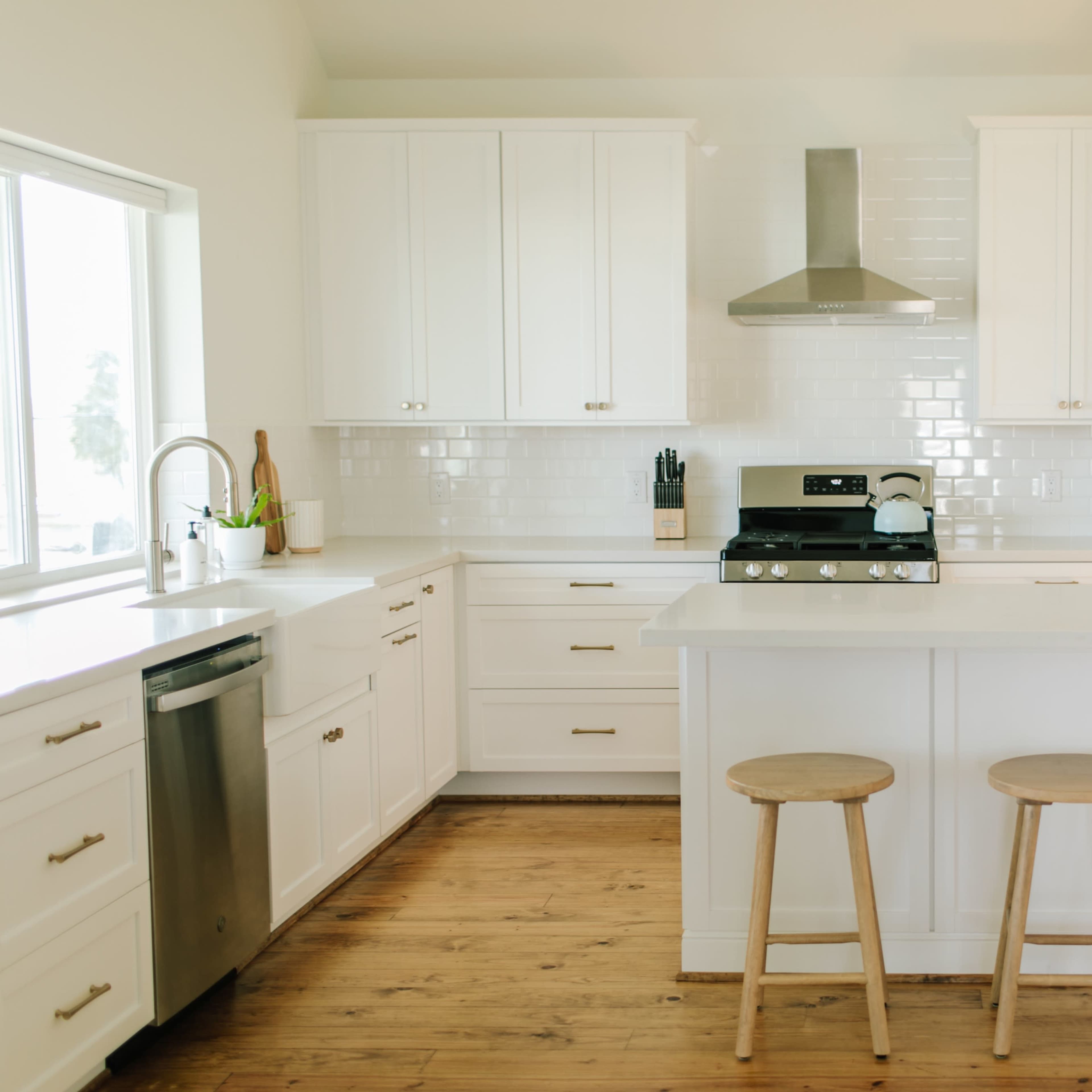 A modern kitchen features white cabinetry, stainless steel appliances, and three wooden stools at a central island.