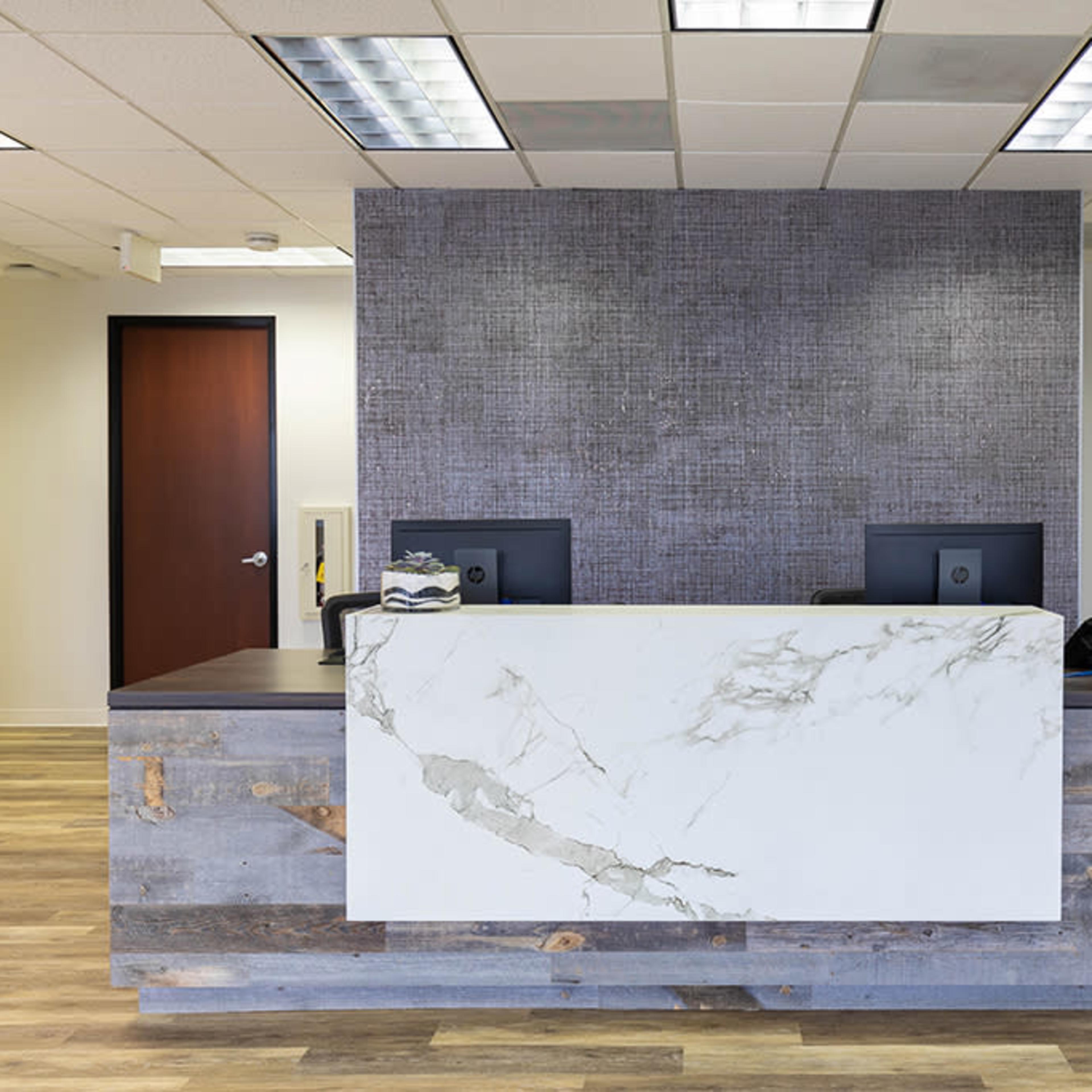 A modern reception area with a marble-topped desk and computer monitors set against a textured gray wall.