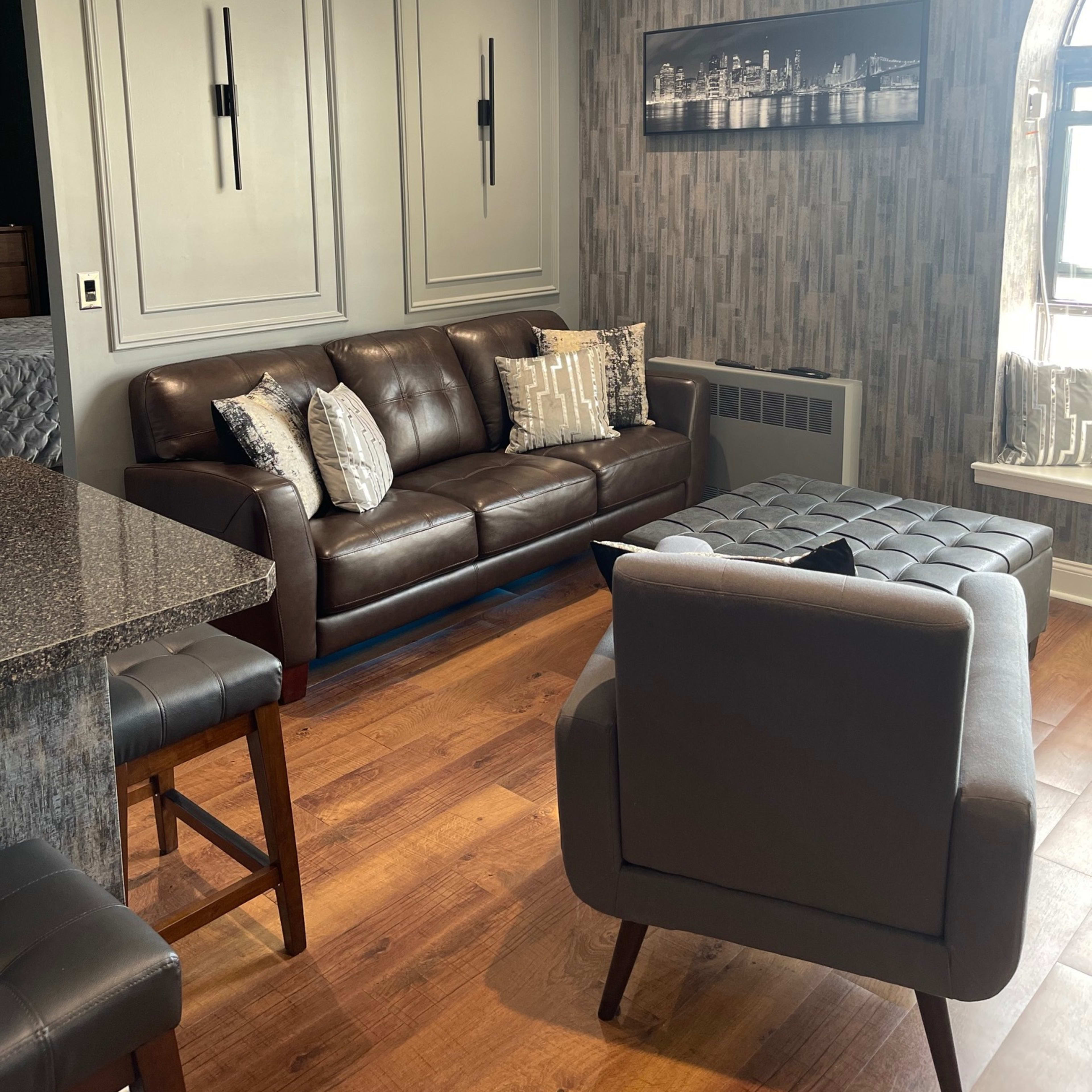 A modern living room featuring a dark leather sofa with decorative pillows, a coffee table, and patterned wallpaper.