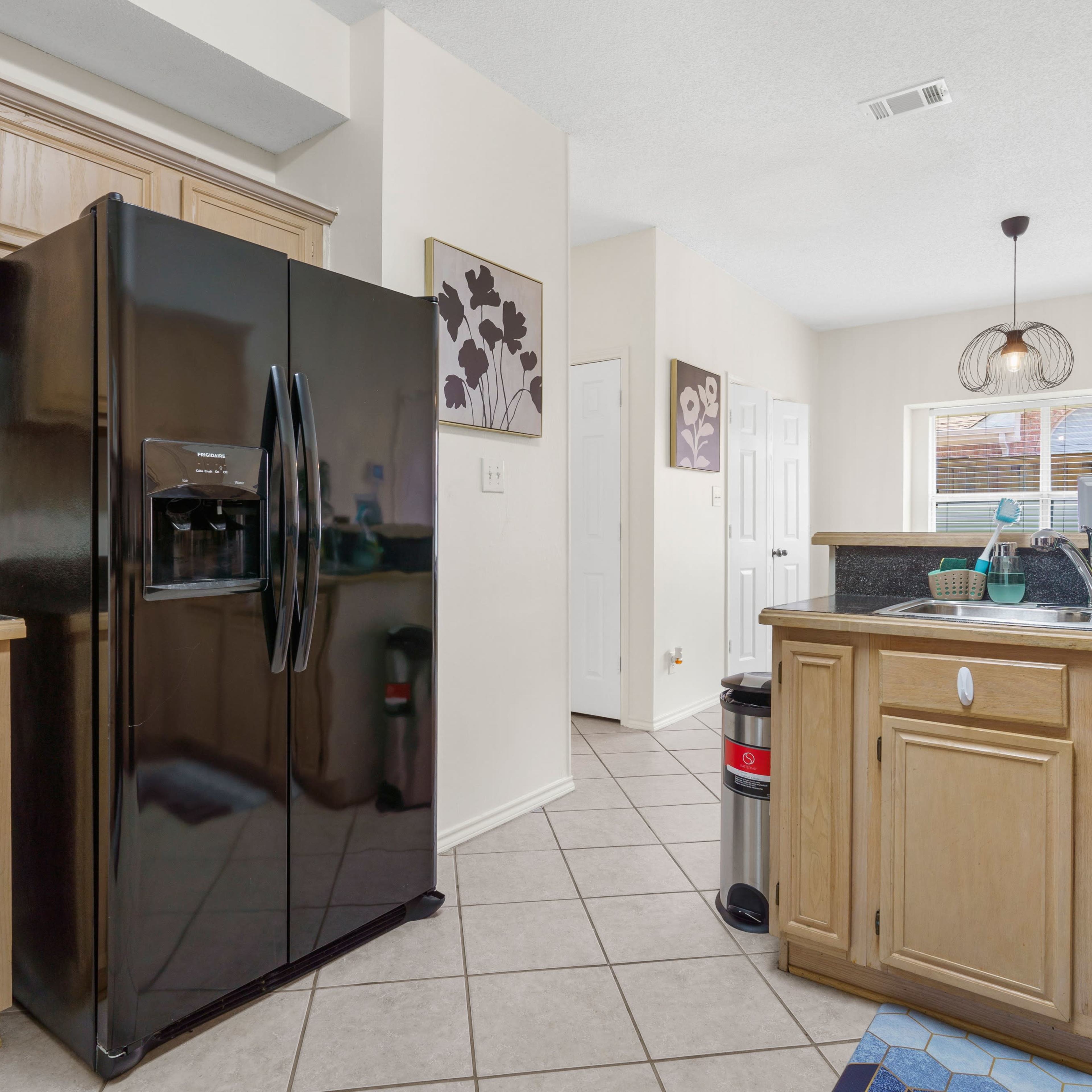 A kitchen featuring a black refrigerator, wooden cabinets, a sink, and tile flooring.