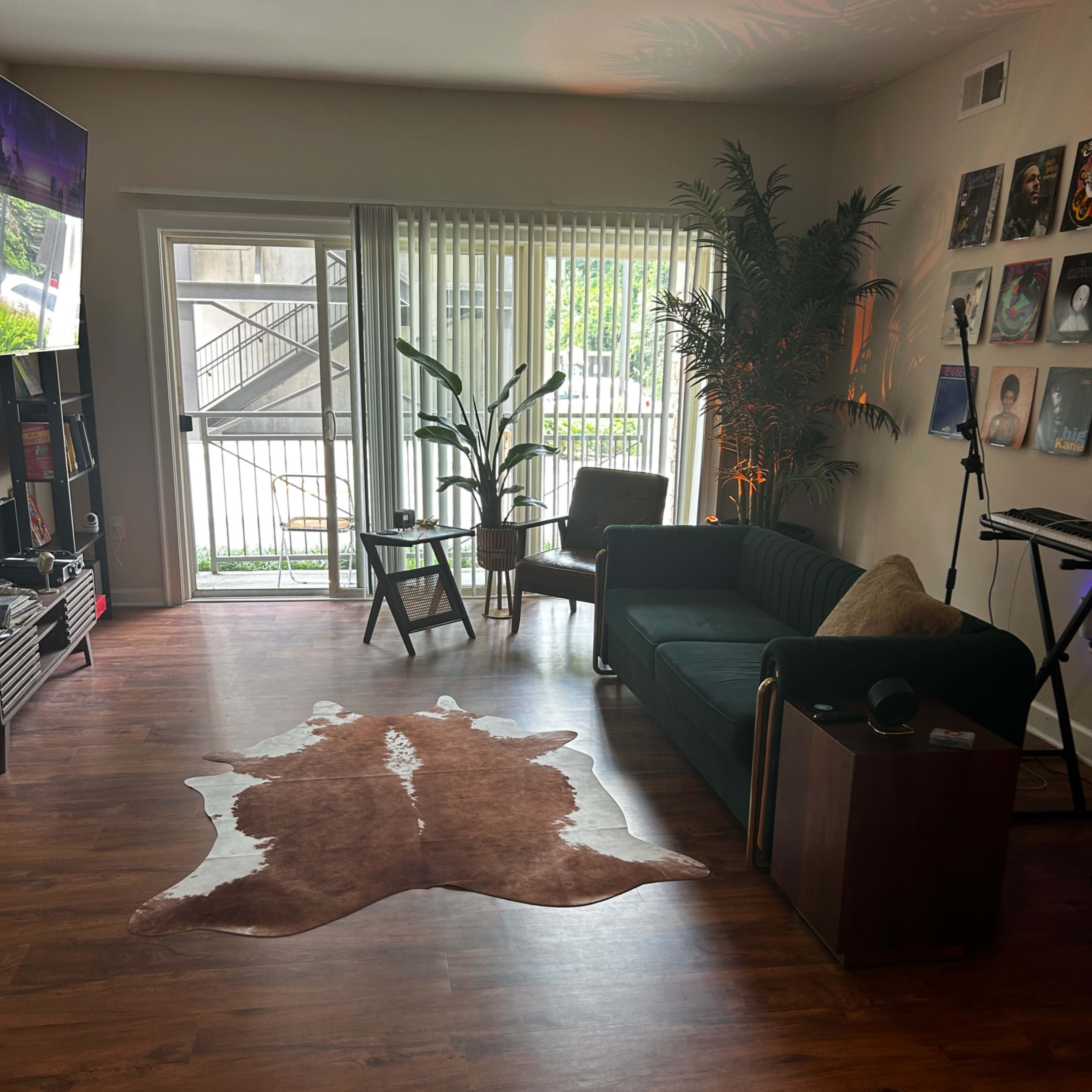 The living room features a dark green couch, a wooden chair, and a rug on the floor, with sliding glass doors leading to an outdoor area.