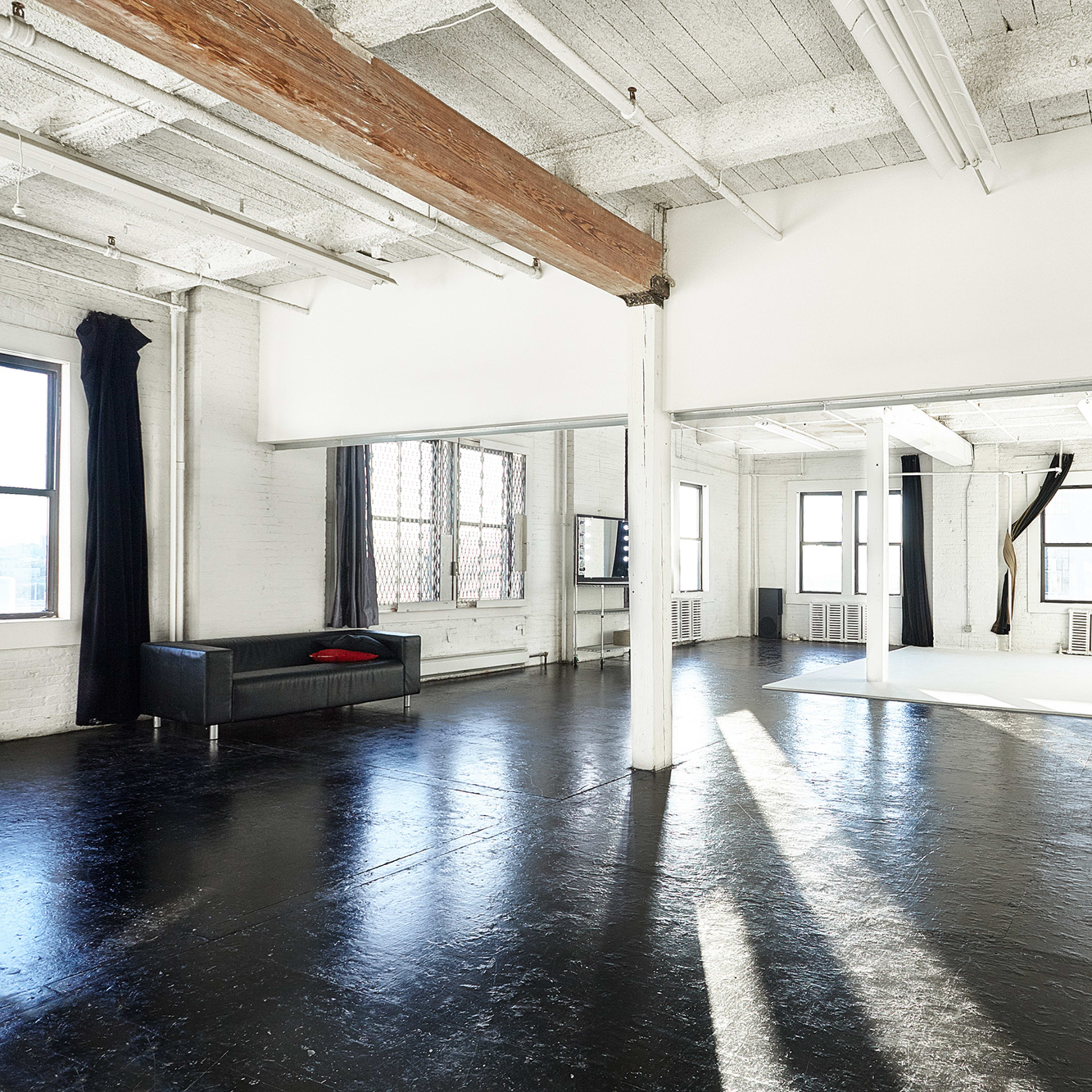 A spacious, modern studio with large windows, polished black floors, and minimal furniture.