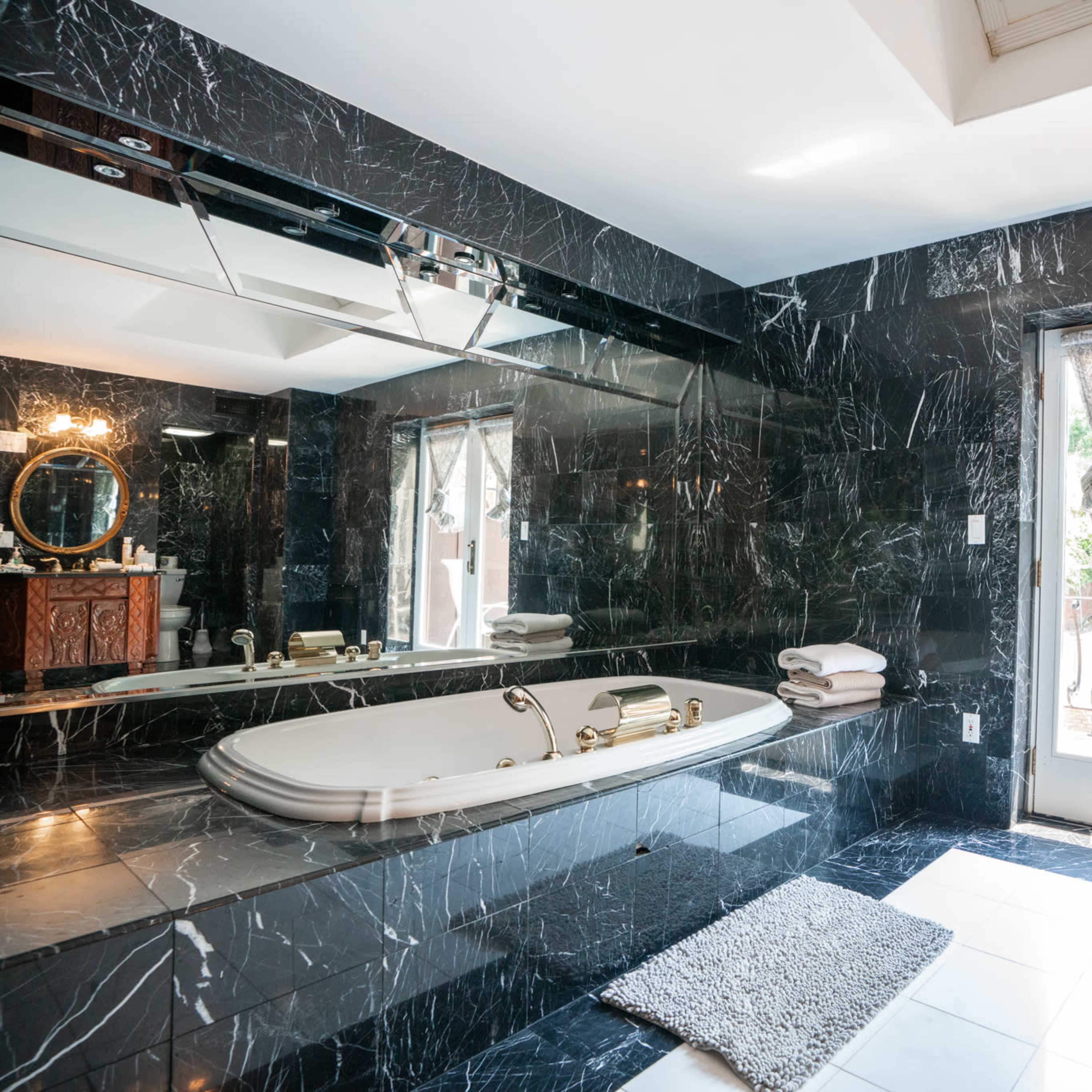 A luxurious bathroom featuring a marble tub, large mirror, and double doors leading to an outdoor area.
