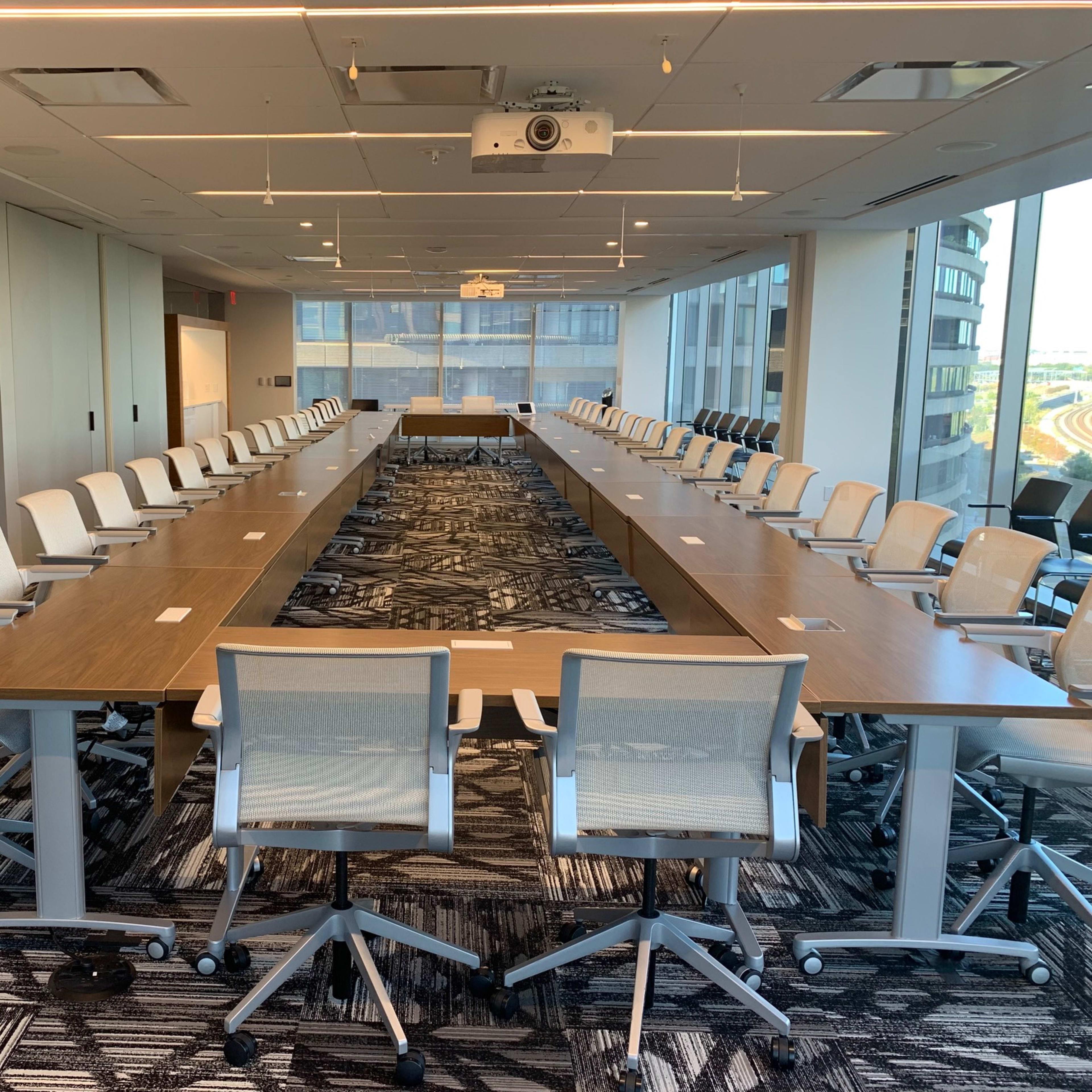 A large conference room with a long, rectangular table surrounded by swivel chairs and large windows providing natural light.