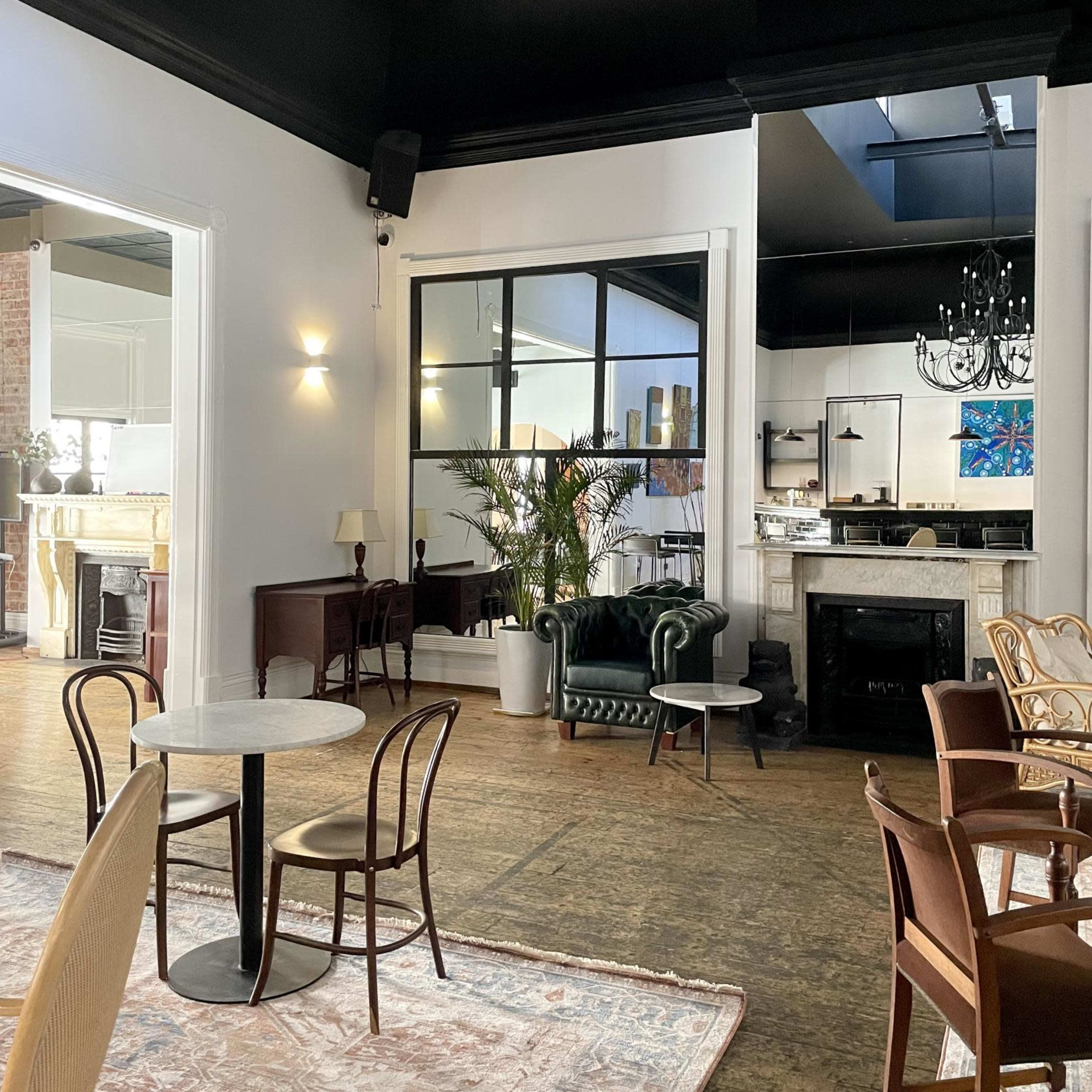 A modern café interior with a mix of dining tables, chairs, and a green velvet couch, featuring large windows and decorative elements.