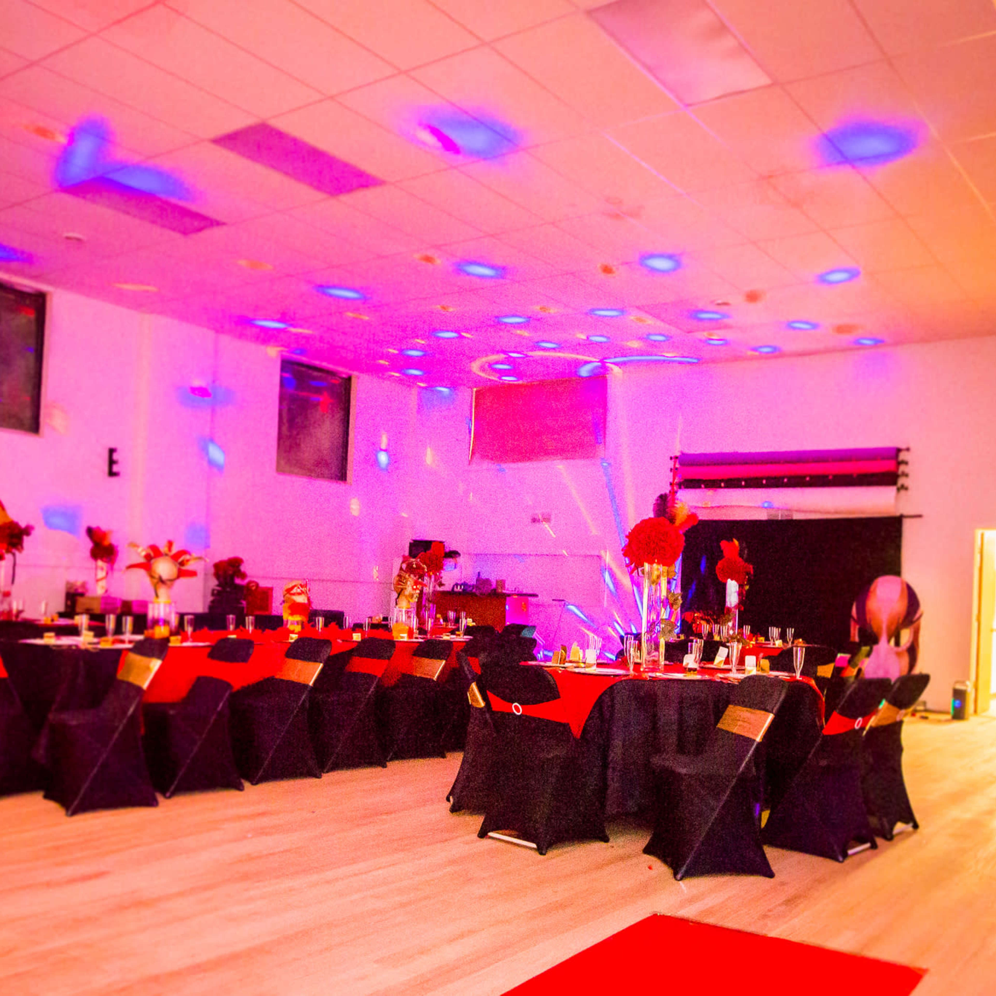 A banquet hall set up for an event, featuring tables decorated with red and black tablecloths, flowers, and ambient lighting.