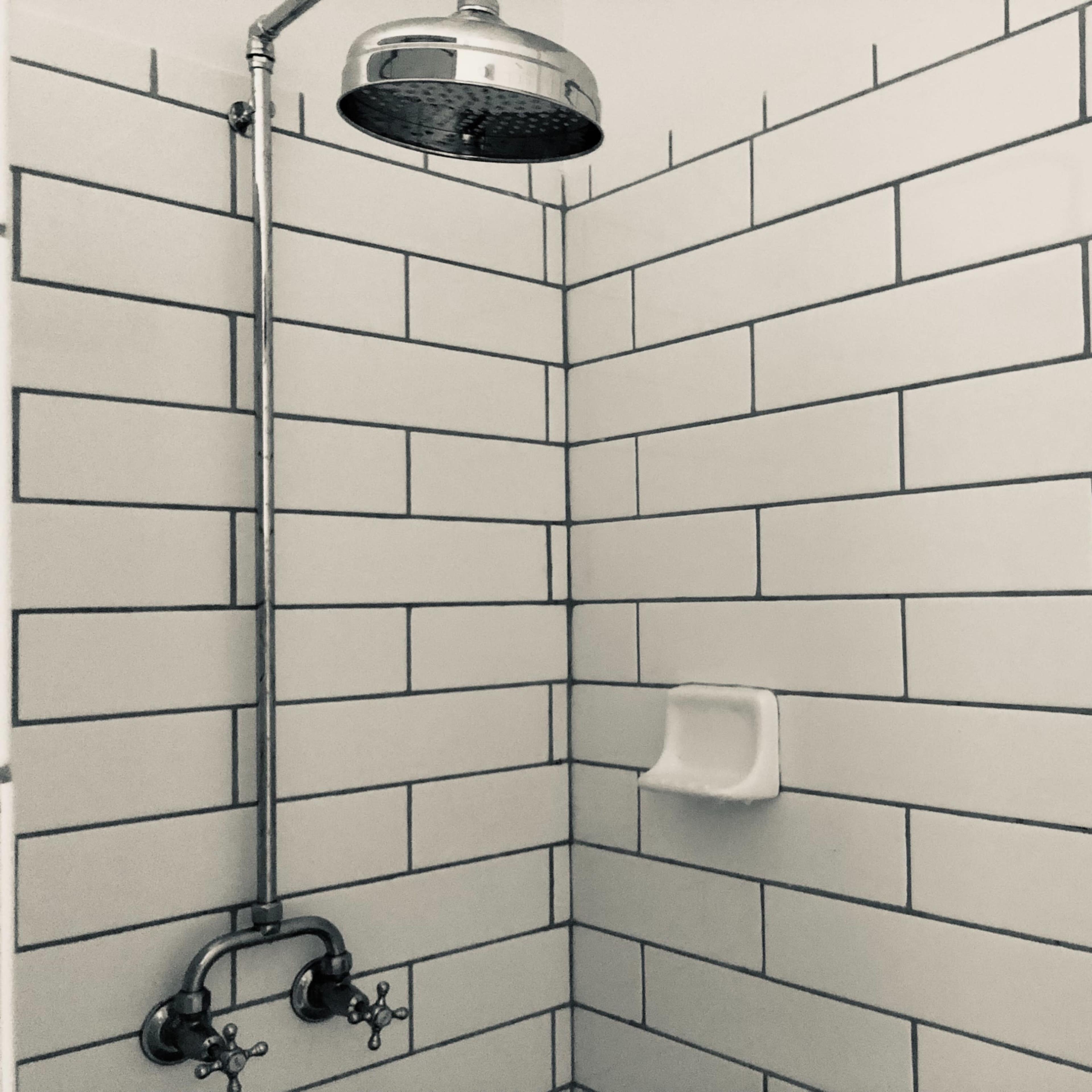A shower with a chrome showerhead mounted above white tiled walls and a small soap shelf.