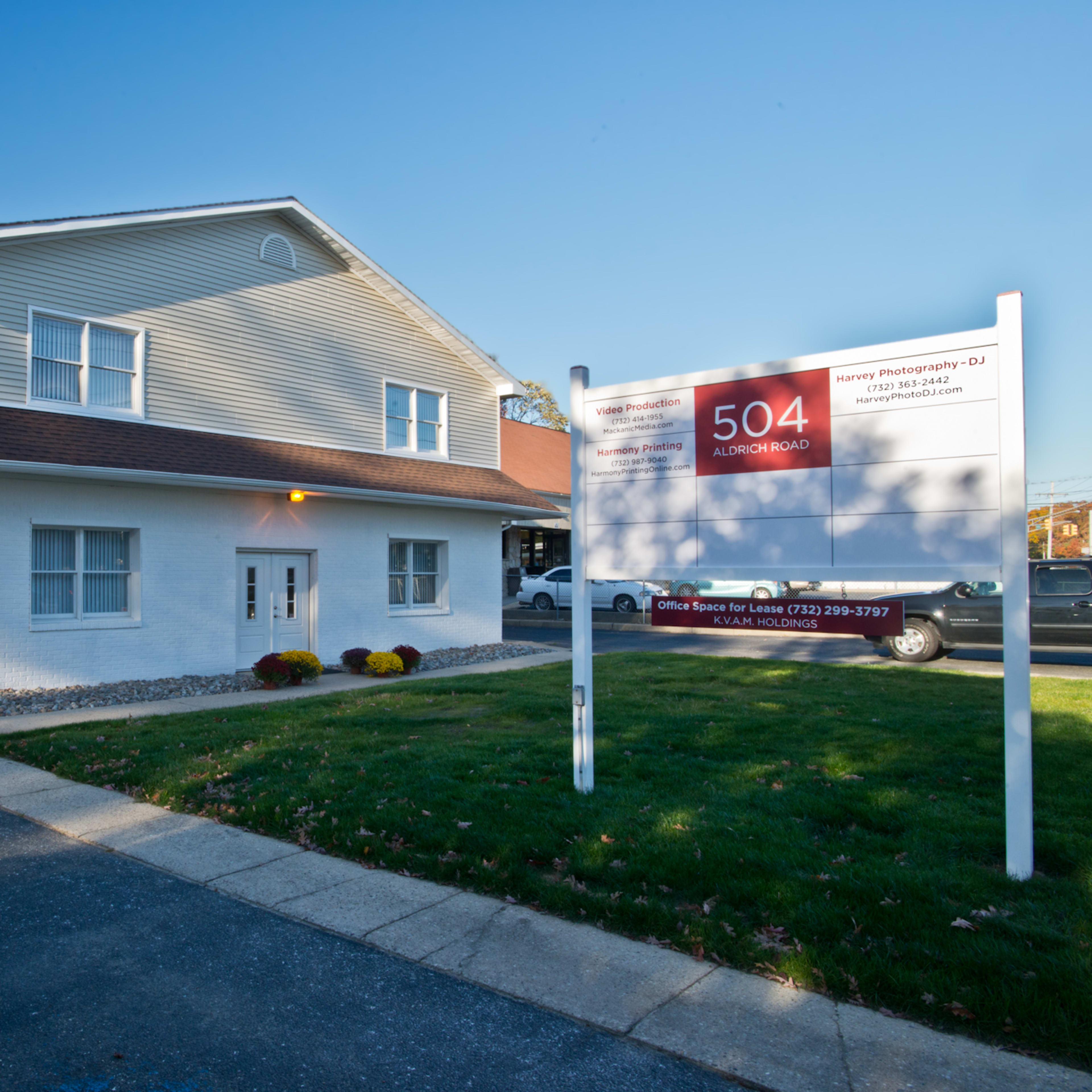 A two-story office building with a white exterior and a large sign displaying the address "504 Aldon Road" in front of it, surrounded by a small lawn and driveway.