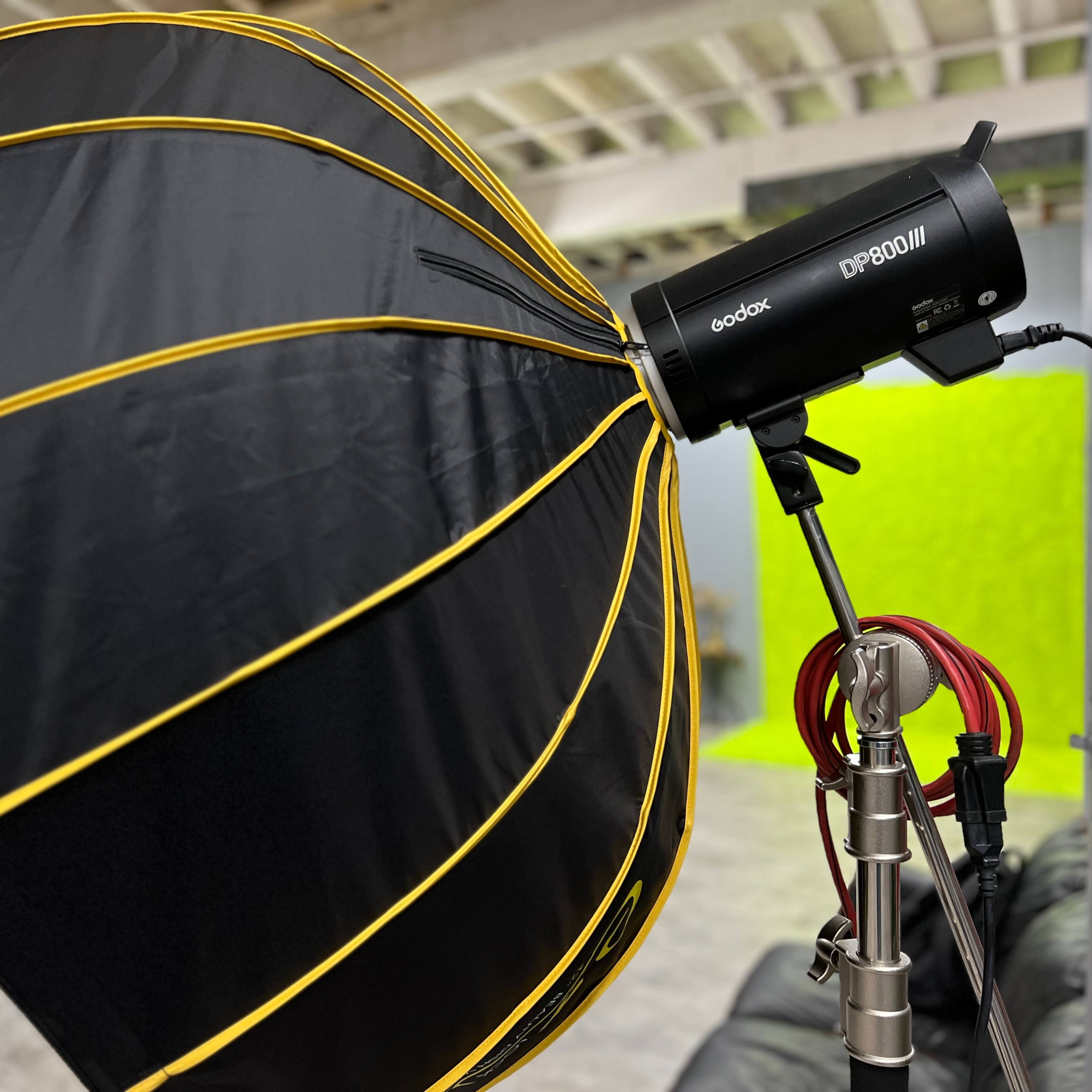 A black and yellow softbox is mounted on a strobe light in a studio with a green backdrop.