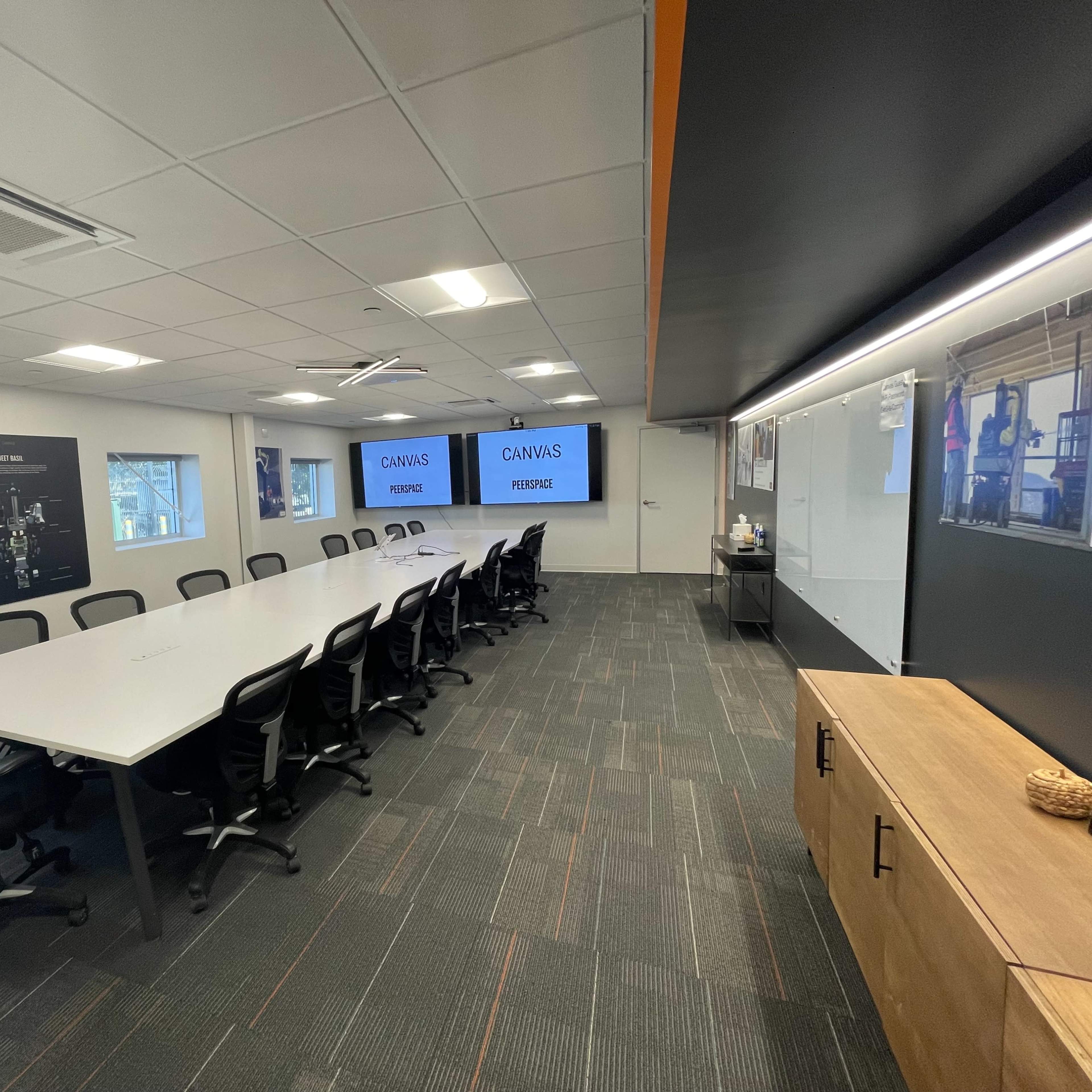 A modern conference room features a long white table surrounded by black chairs, with two large screens displaying the words "CAHNS" and "FIREZE" on the walls.
