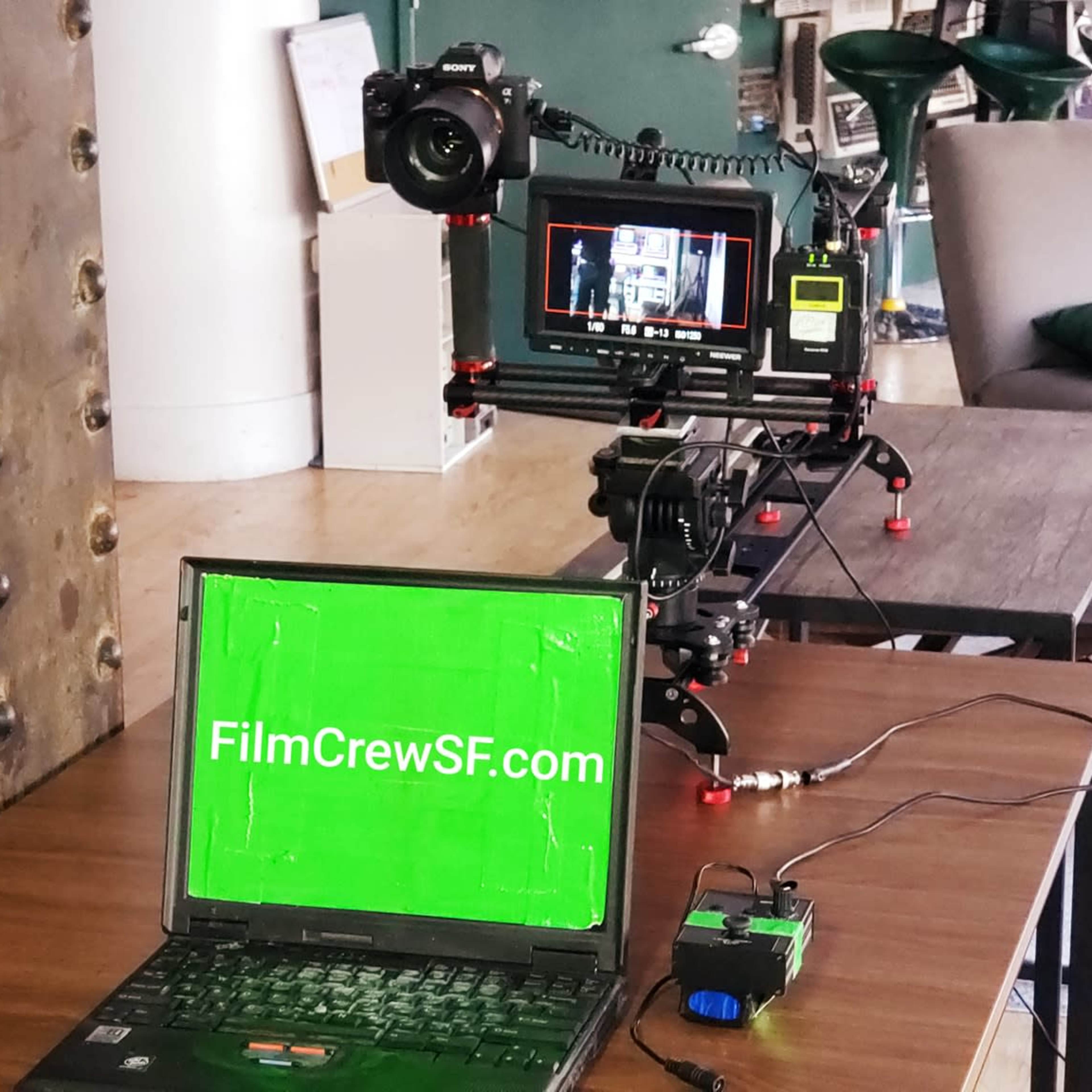 A camera setup is shown on a table, including a laptop with a green screen displaying "FilmCrewSF.com" and a monitor connected to the camera.