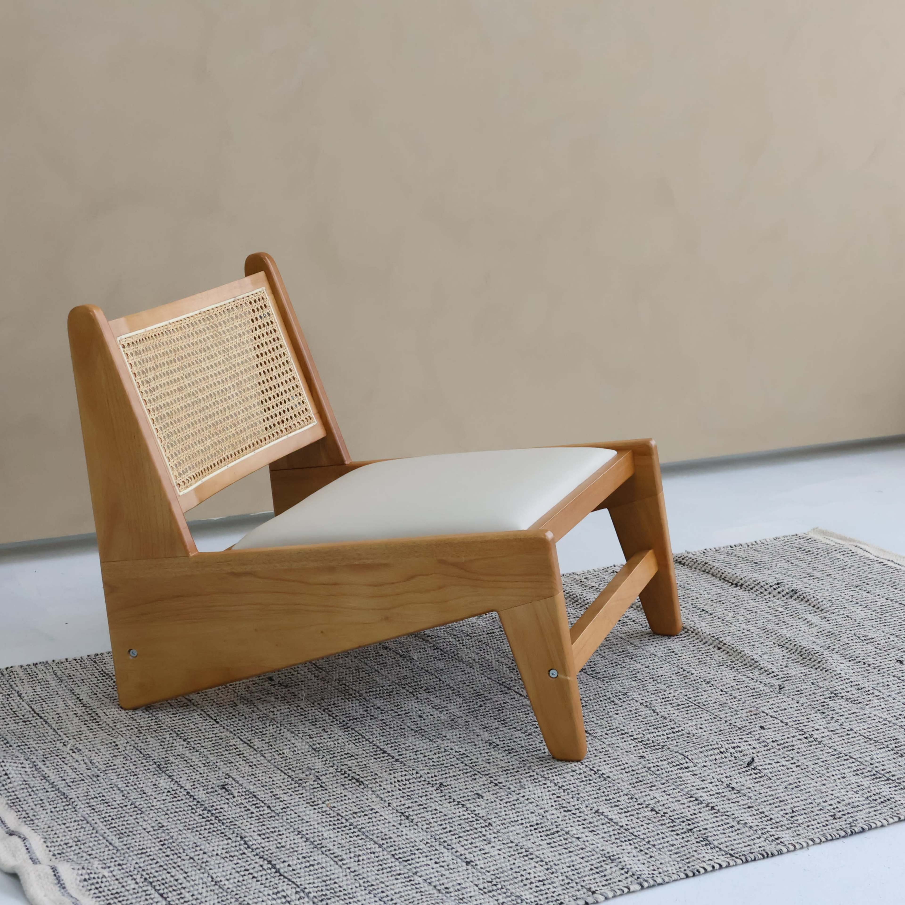 A wooden chair with a cane backrest and a cushioned seat is placed on a textured rug in a softly lit room.