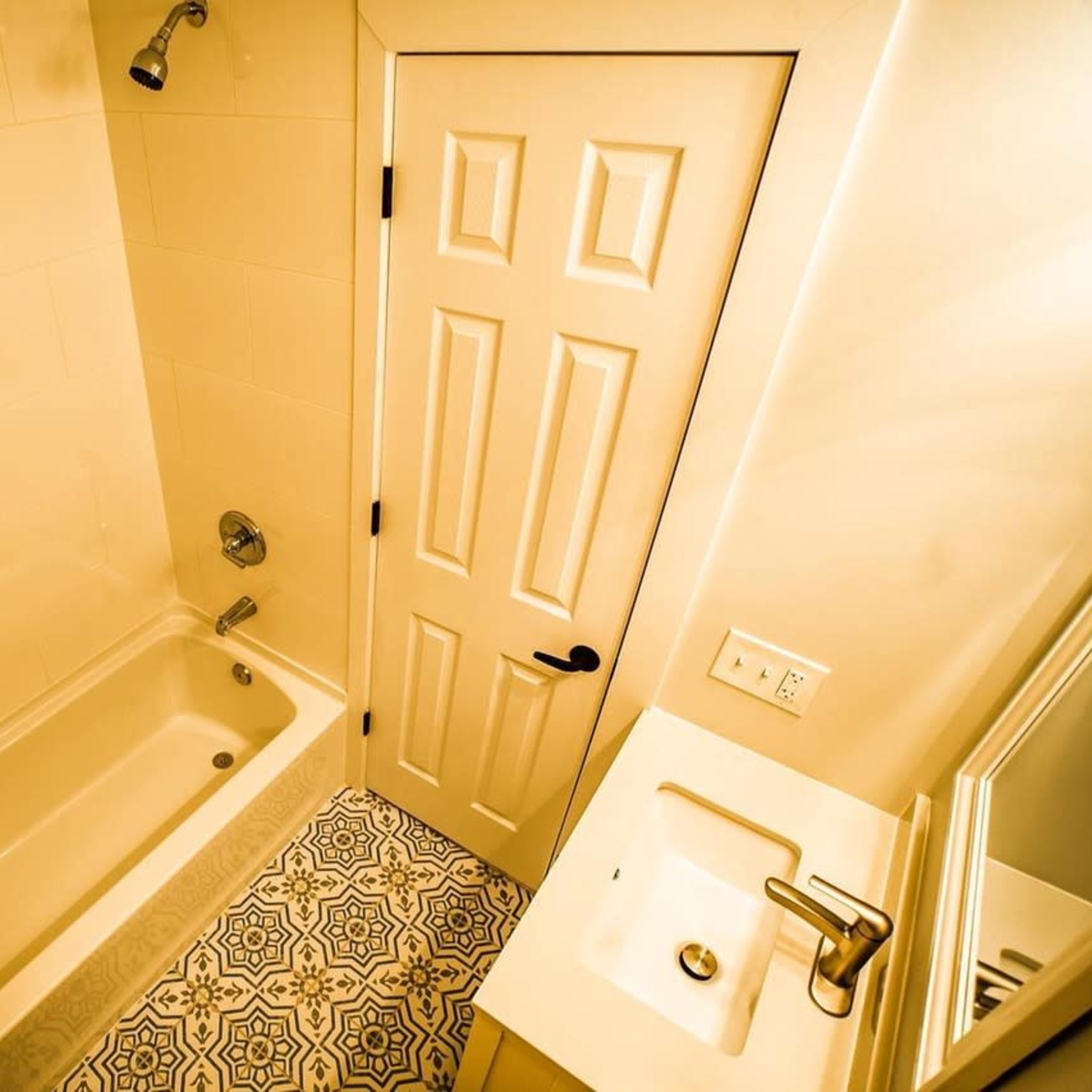A small bathroom featuring a bathtub, a sink, and decorative patterned tiles on the floor.