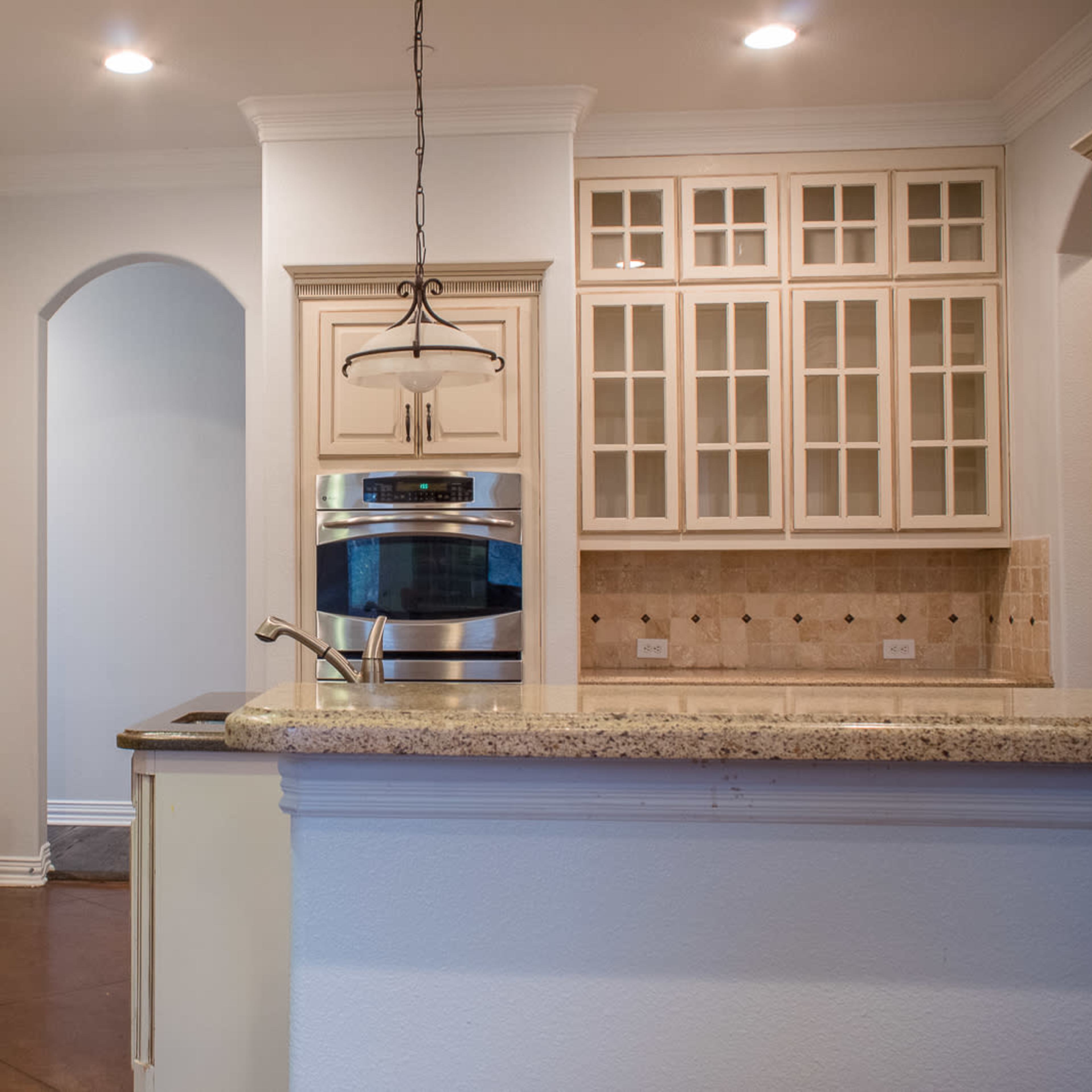 A modern kitchen features light cabinetry, a granite countertop, and stainless steel appliances, with an archway leading to another room.
