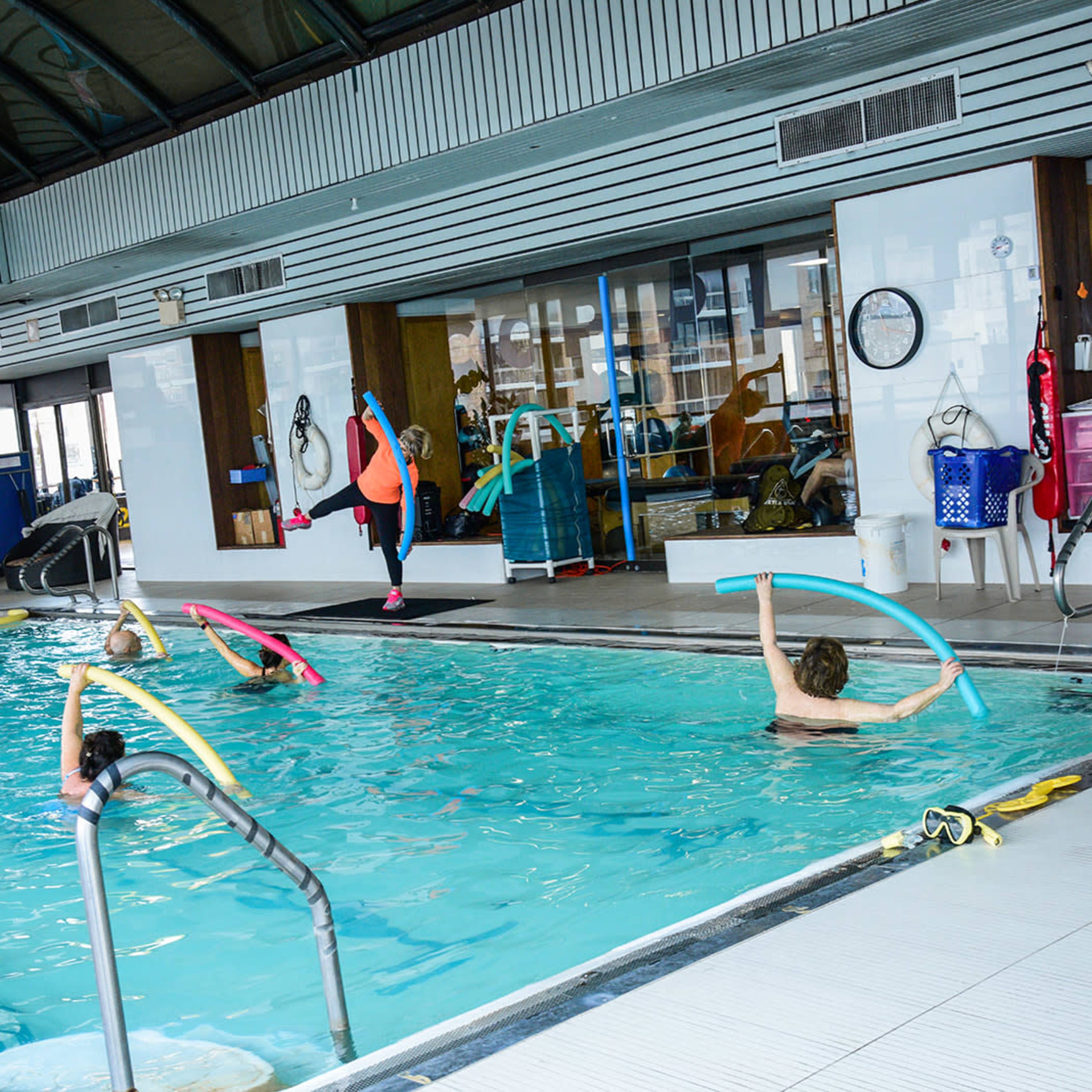 A group of people participates in a water aerobics class inside a pool facility.