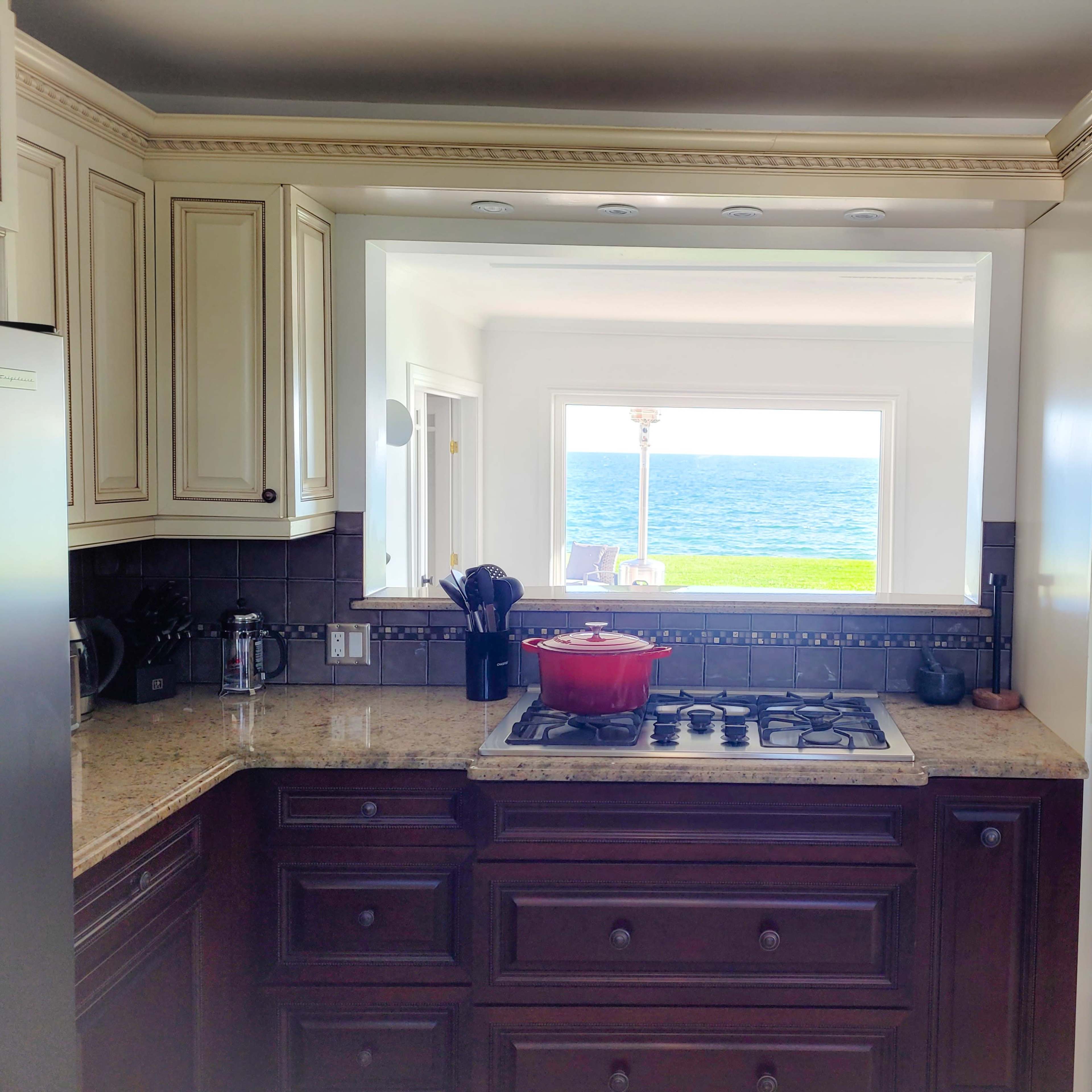 A kitchen with dark wood cabinets and granite countertops has a view of the ocean through a large window.