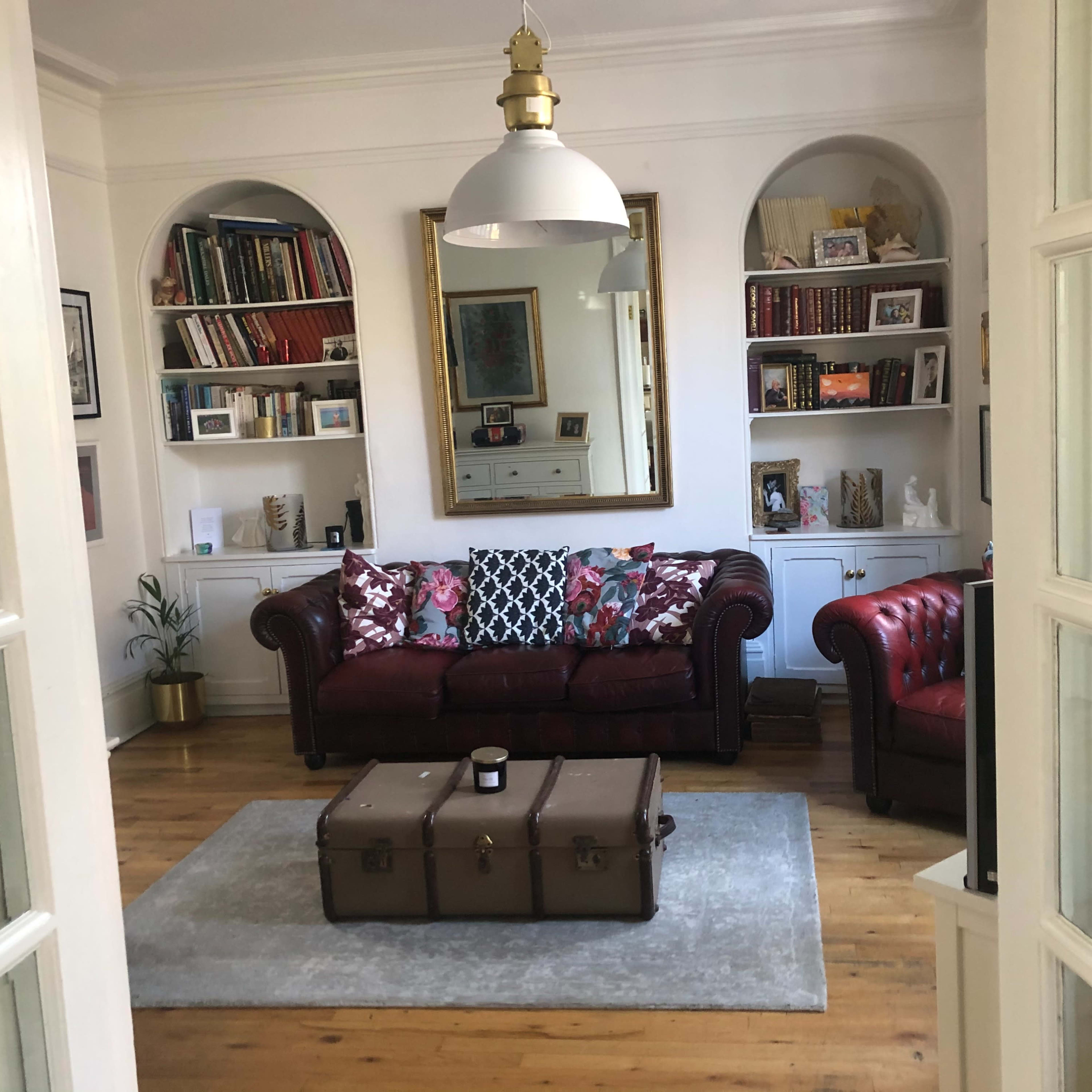 A living room with a red leather sofa, a coffee table, and bookshelves filled with books and decorative items.