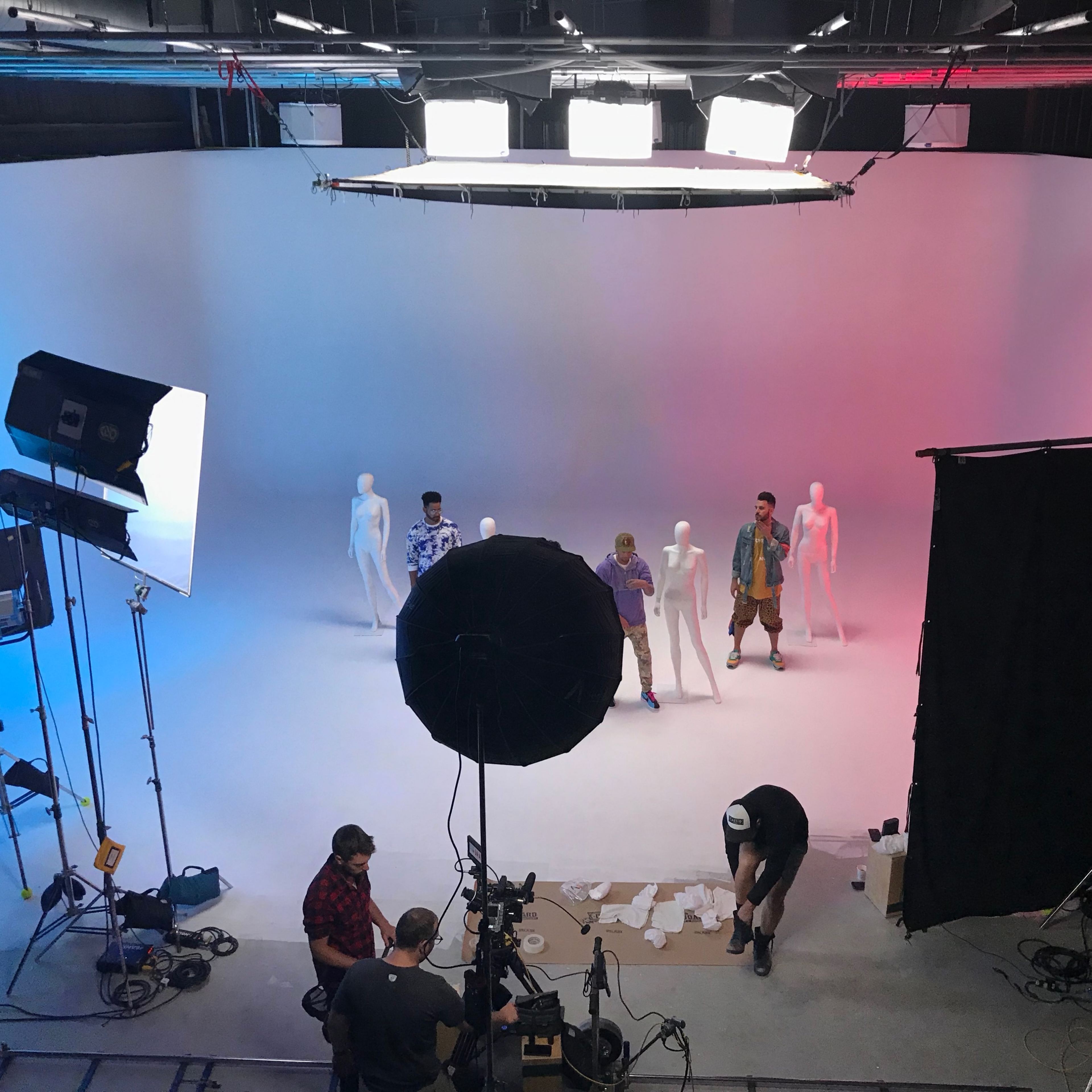 A group of four individuals stands on a stage with white and colored backgrounds, accompanied by several mannequins and studio lighting equipment.