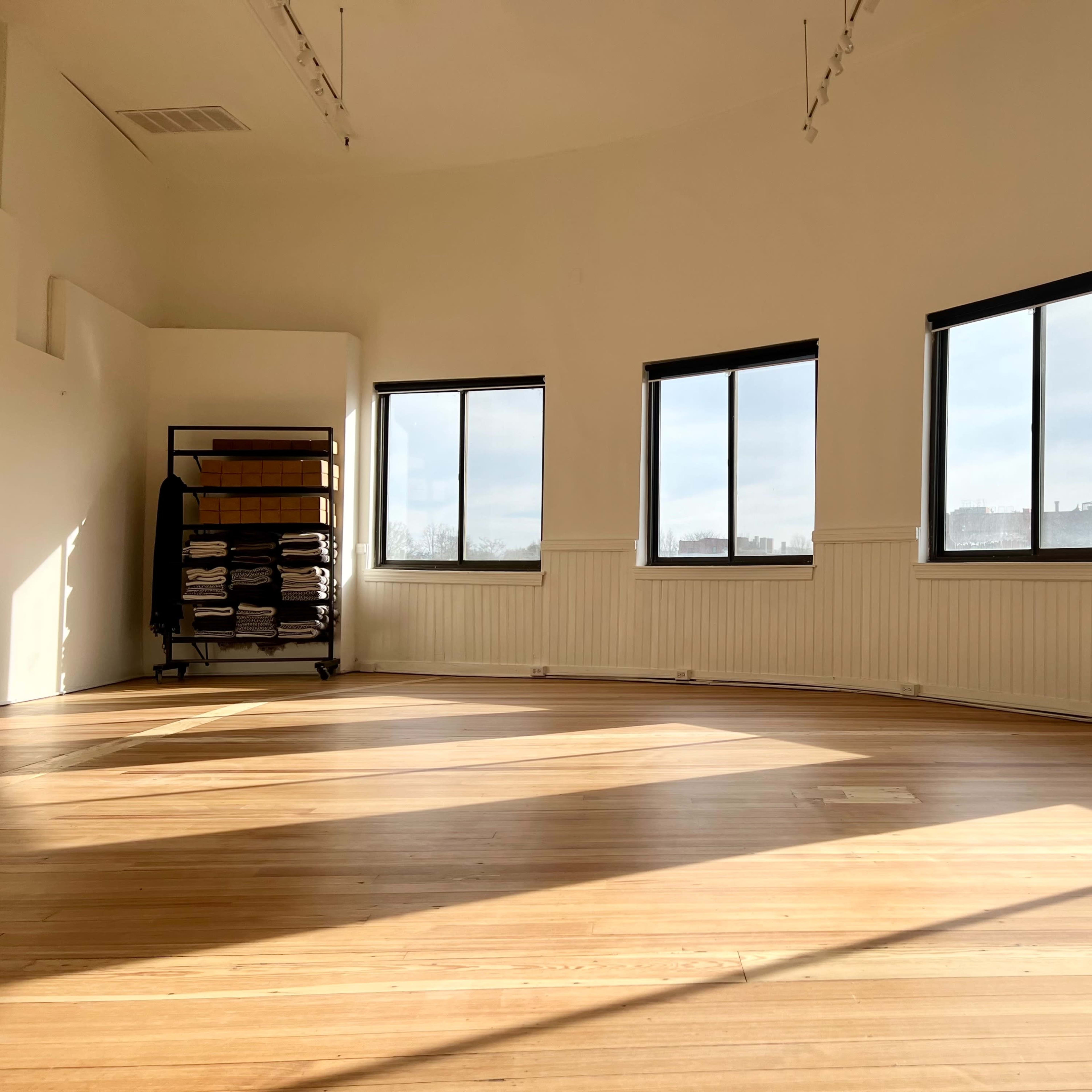 A spacious, well-lit room with wooden flooring and large windows, complemented by a cart of neatly stacked towels in the corner.