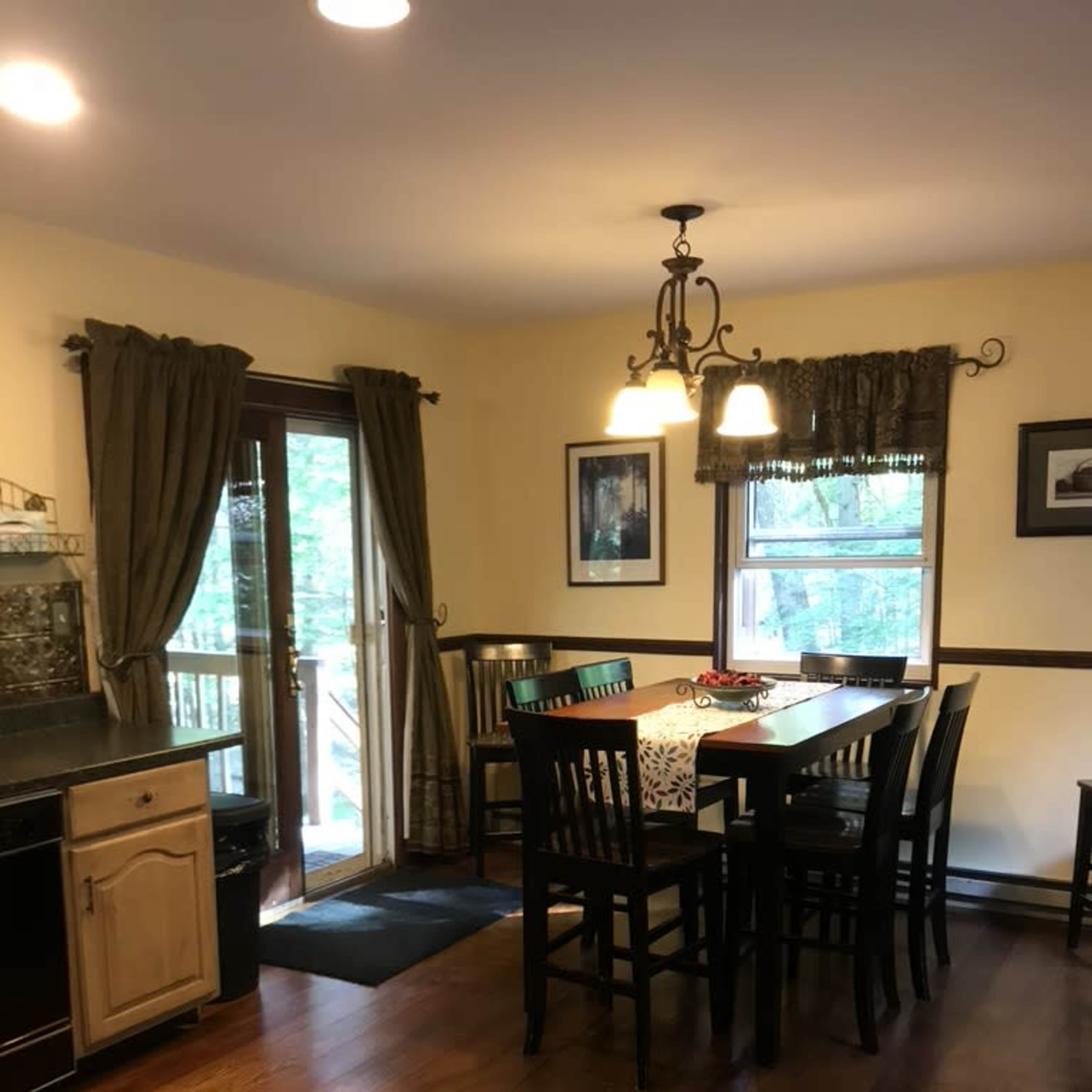 A kitchen with a large dining table, dark wooden chairs, and a door leading outside, illuminated by pendant lights.