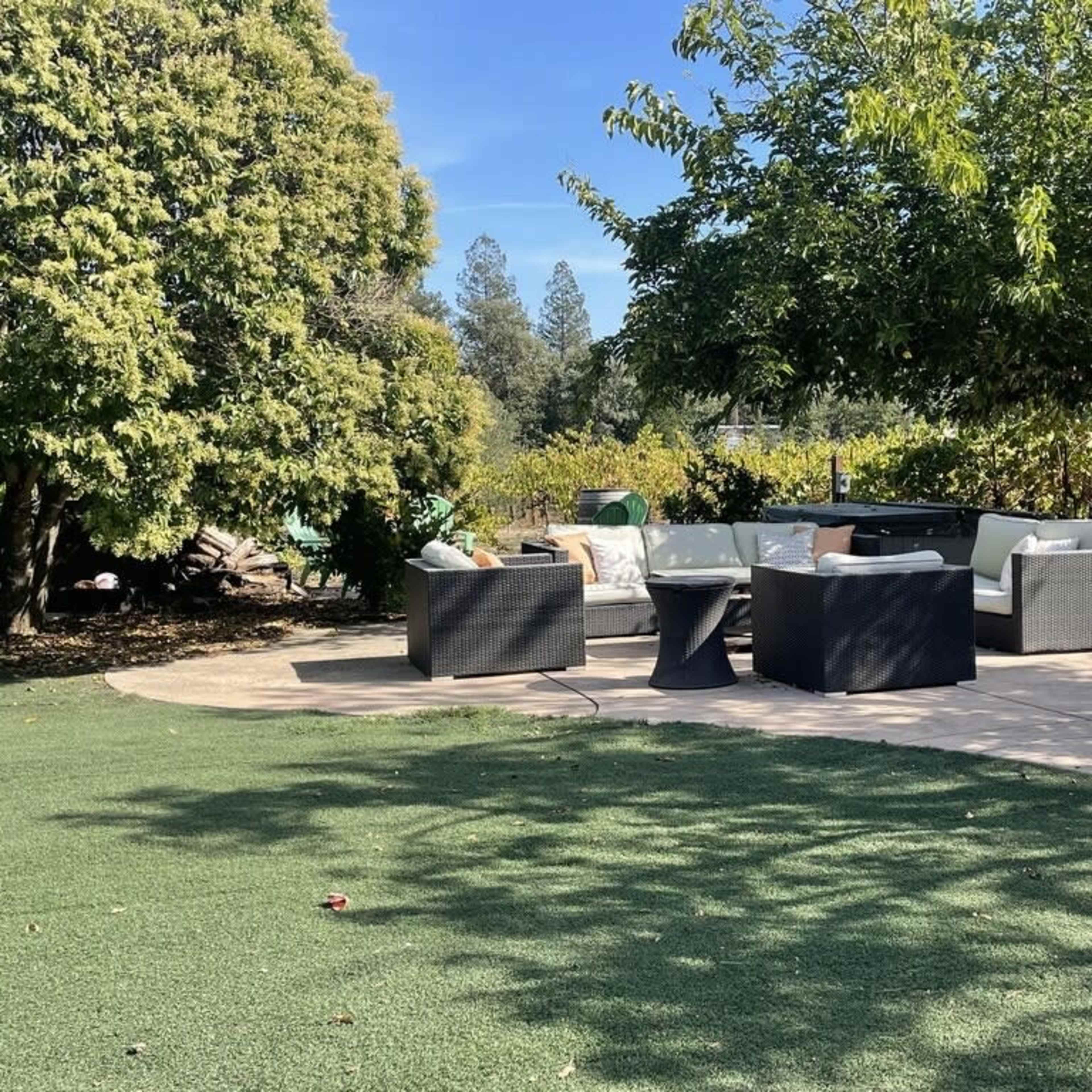 A patio area features a seating arrangement with four chairs and a table, surrounded by greenery and trees.