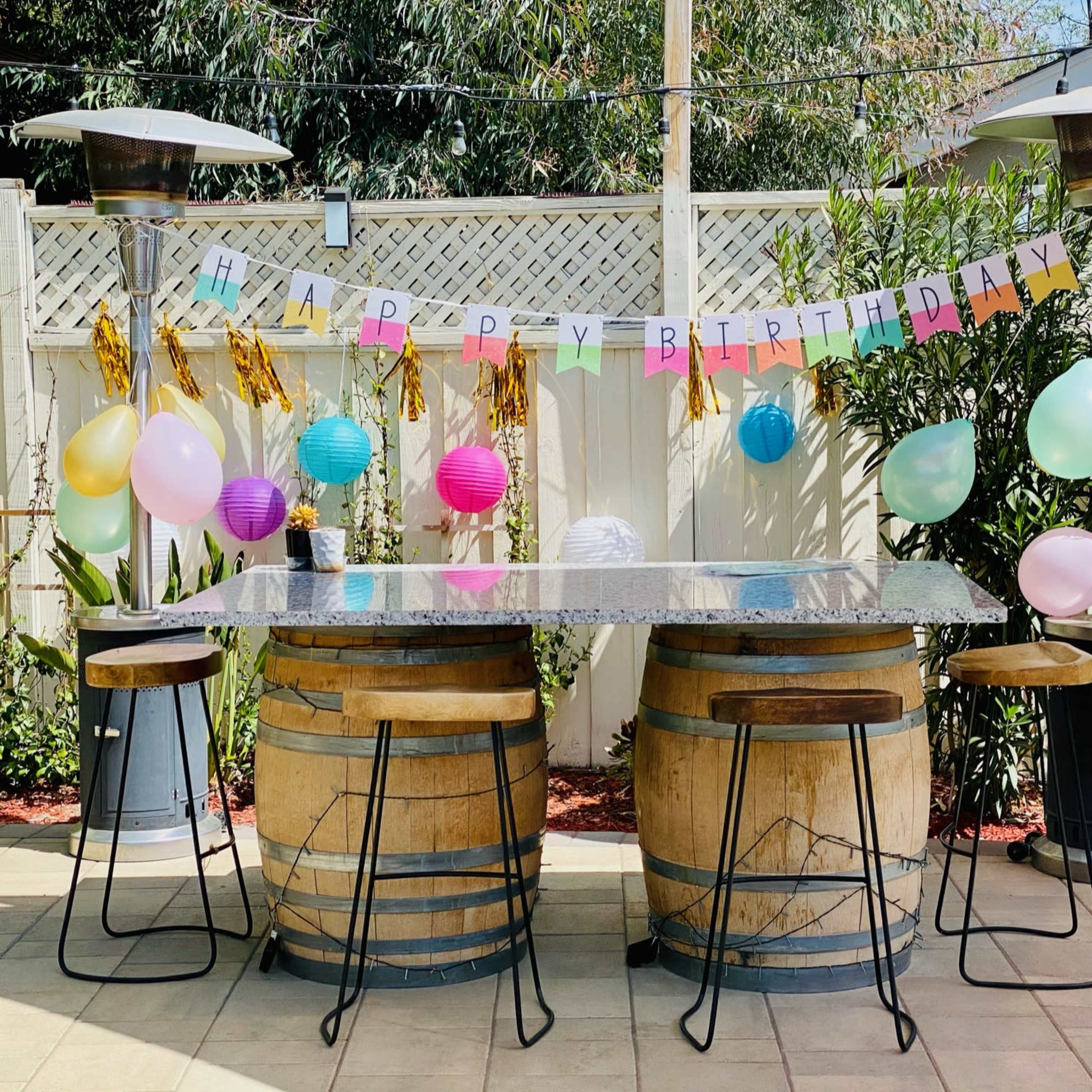 A festive outdoor bar setup with a "Happy Birthday" banner, colorful balloons, and decorative lanterns.