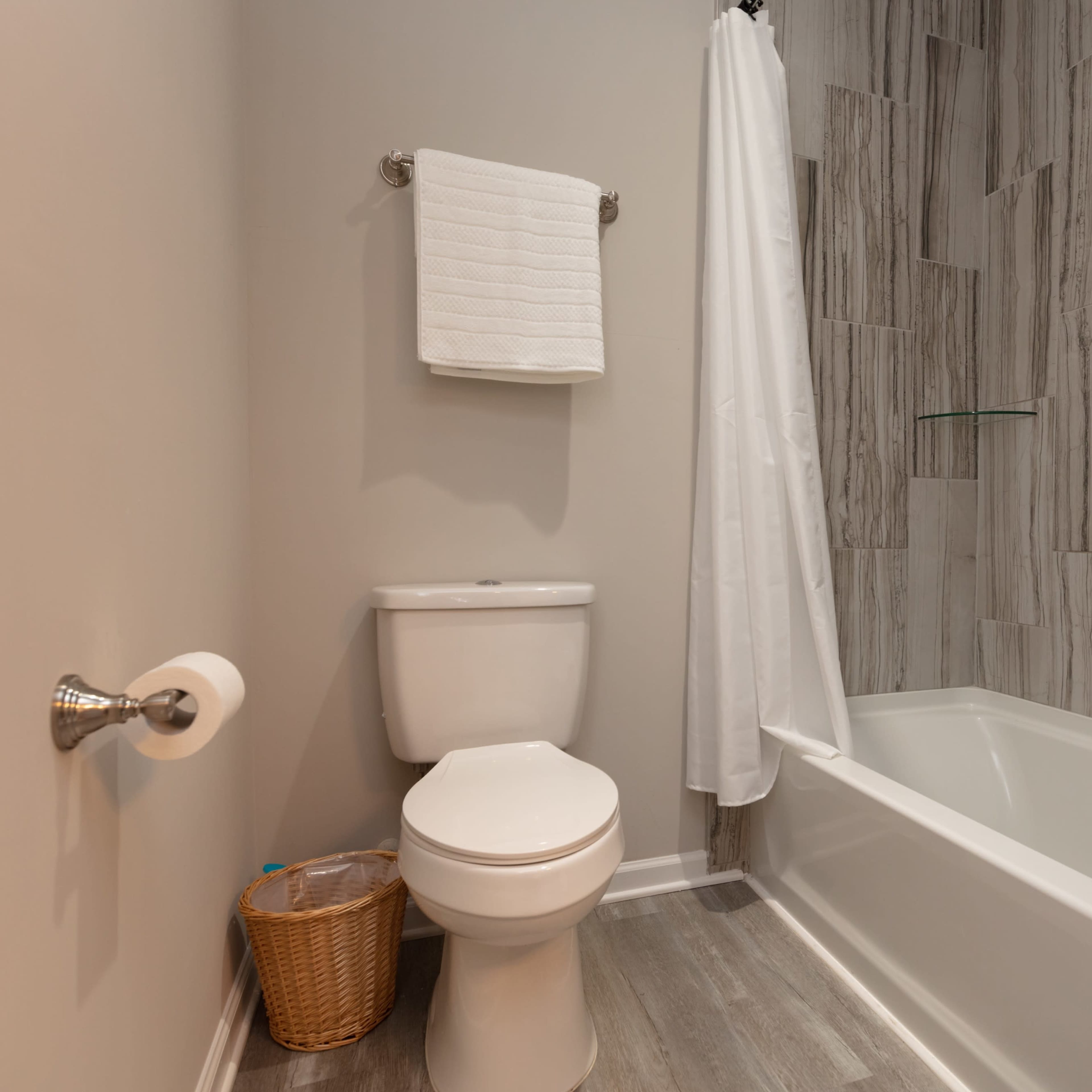 A clean bathroom featuring a toilet, a bathtub with a shower curtain, and a towel rack with two white towels.