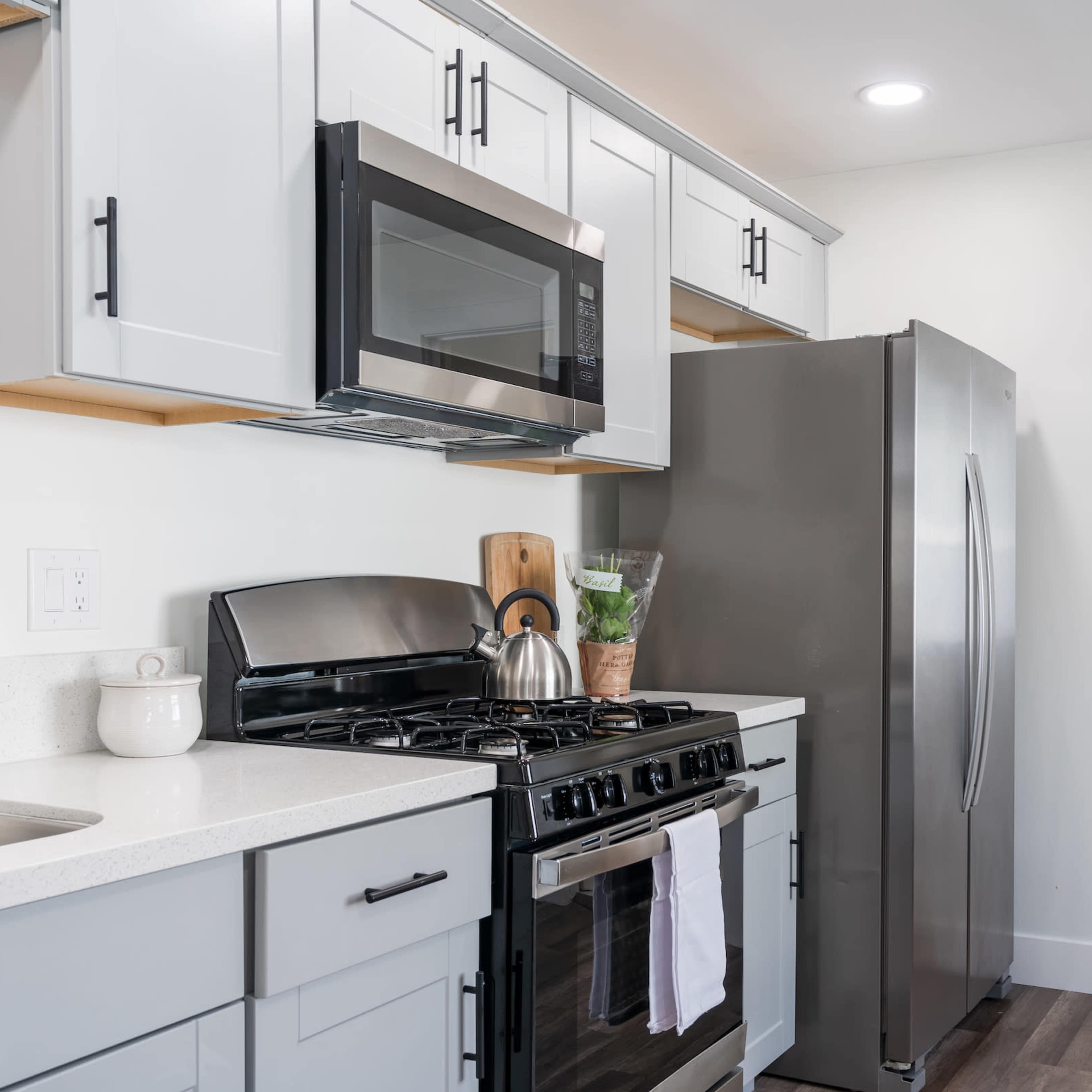 A modern kitchen with gray cabinets, stainless steel appliances, and a small adjacent bathroom visible through an open door.