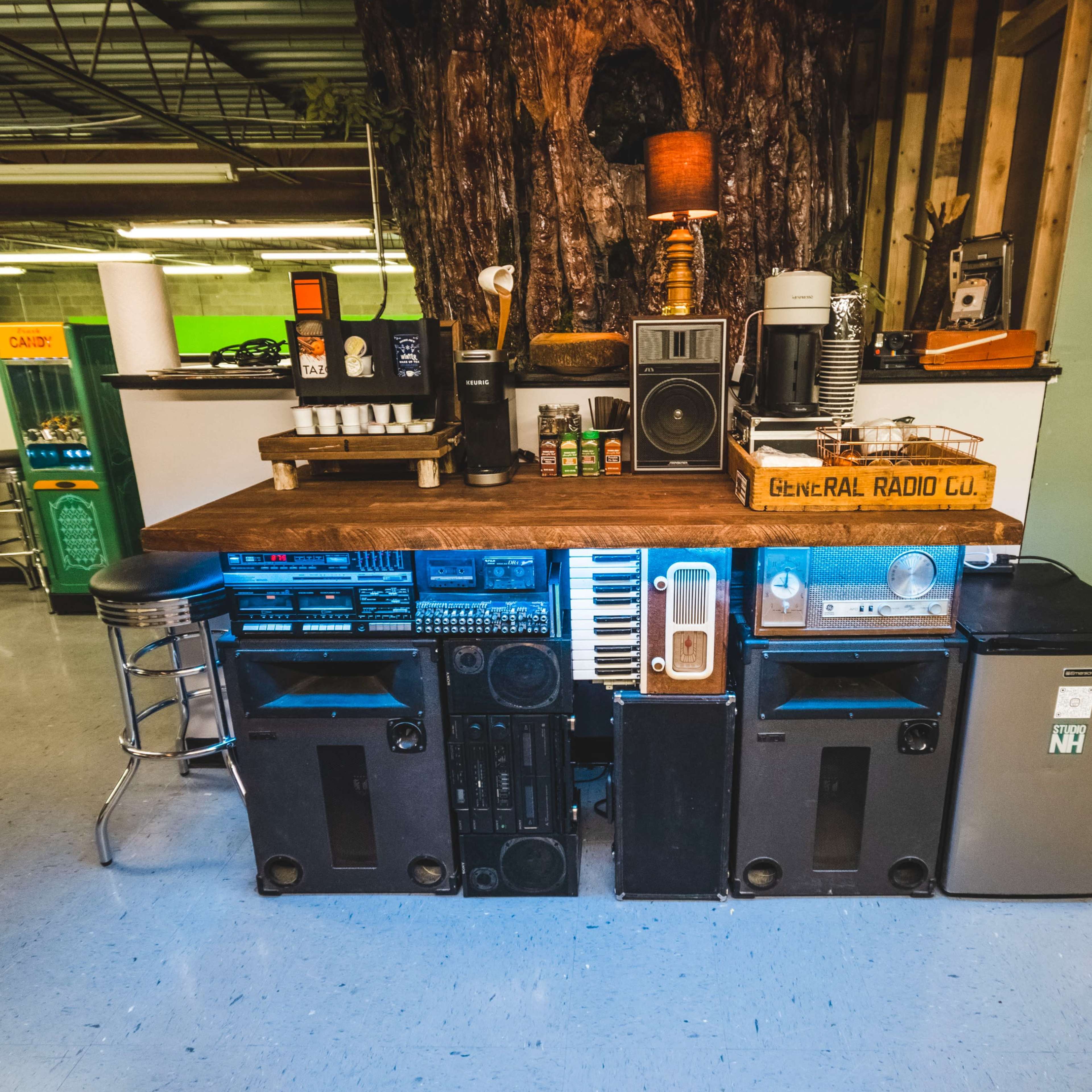 A cluttered counter arrangement made from various audio equipment, appliances, and a wooden tabletop.