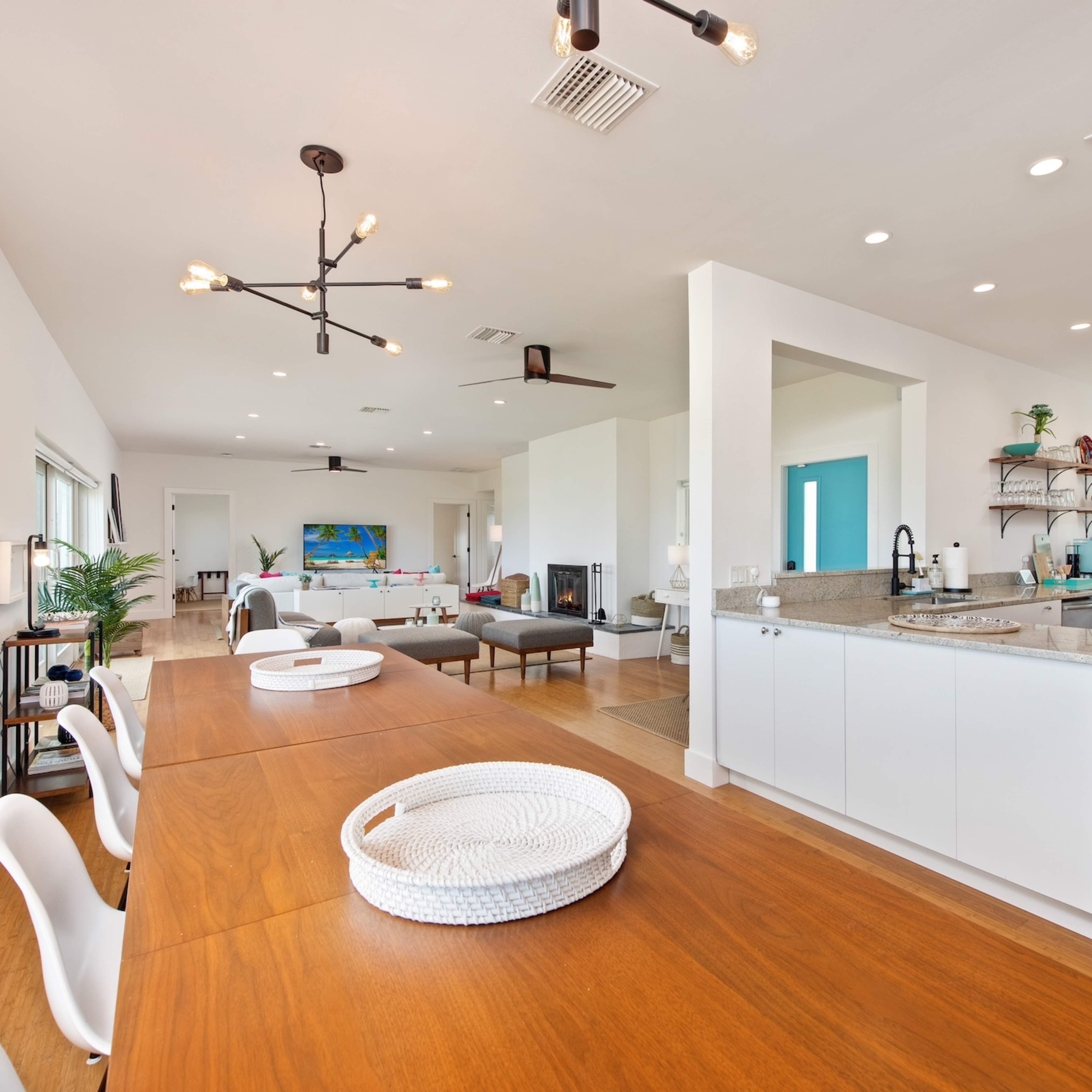 A spacious modern interior with a dining area leading into an open kitchen and living space, featuring large windows and light-colored walls.