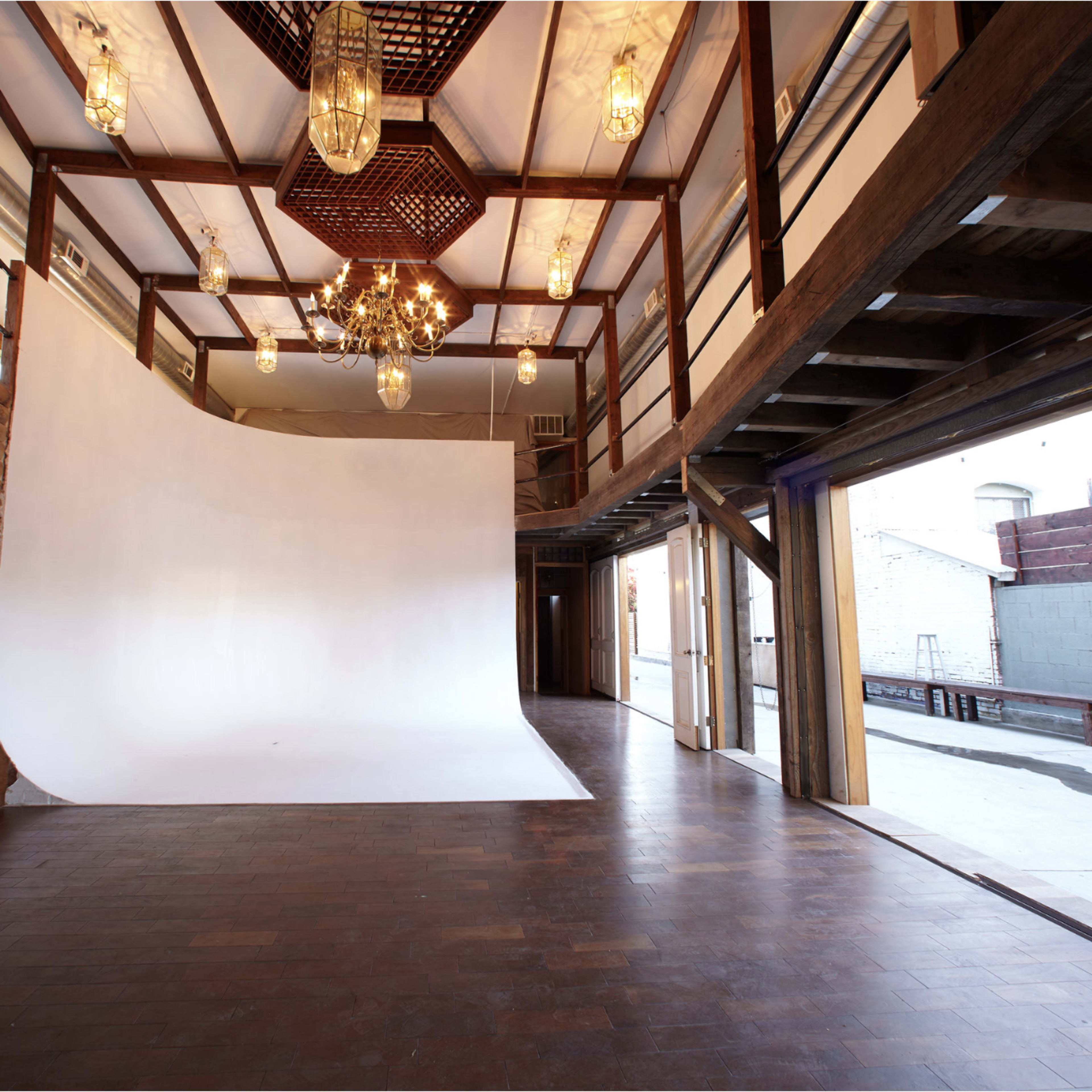 A spacious photography studio with a white backdrop, wooden beams, and hanging light fixtures.