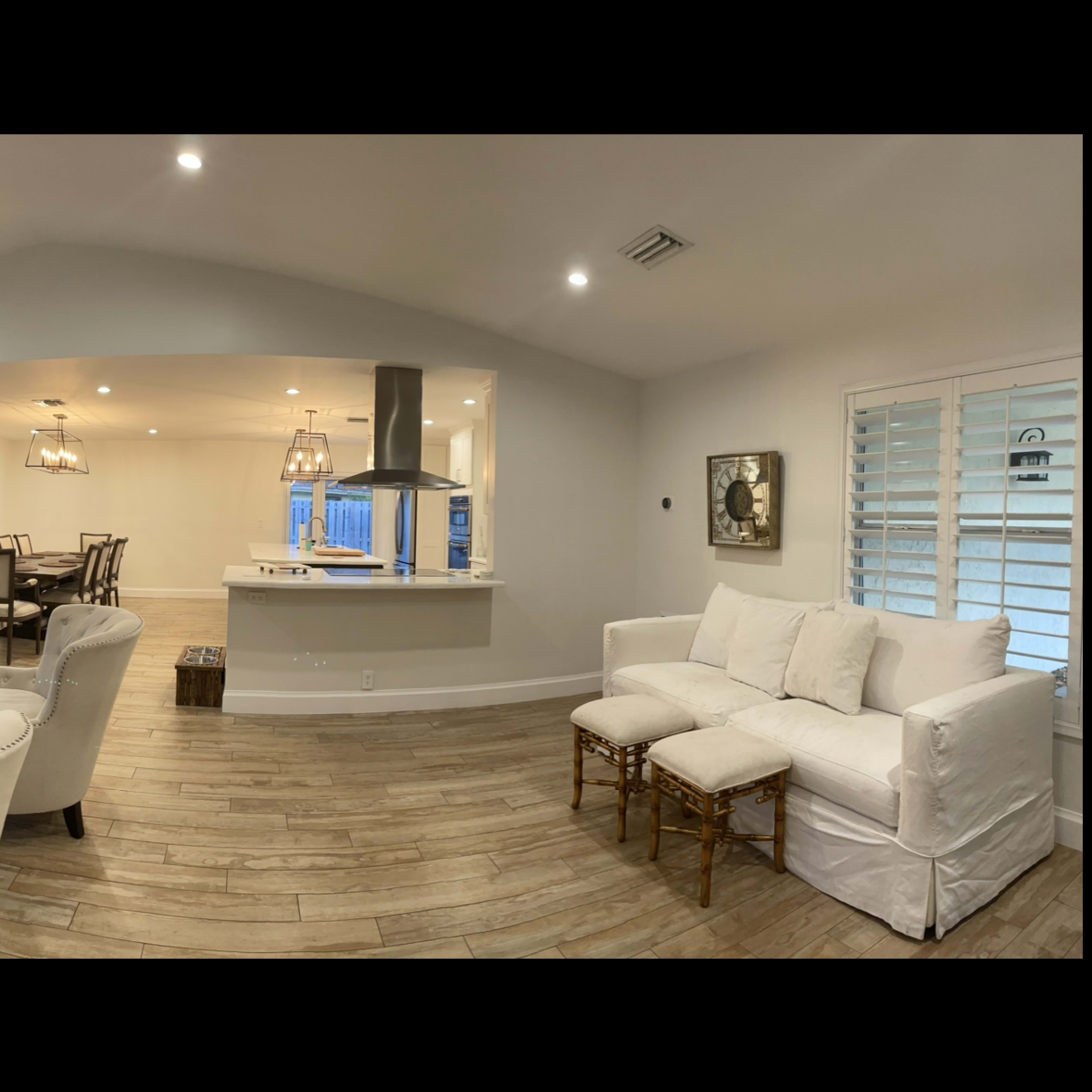A spacious, modern living room and kitchen area with light-colored walls, a large sofa set, and a ceiling fan.