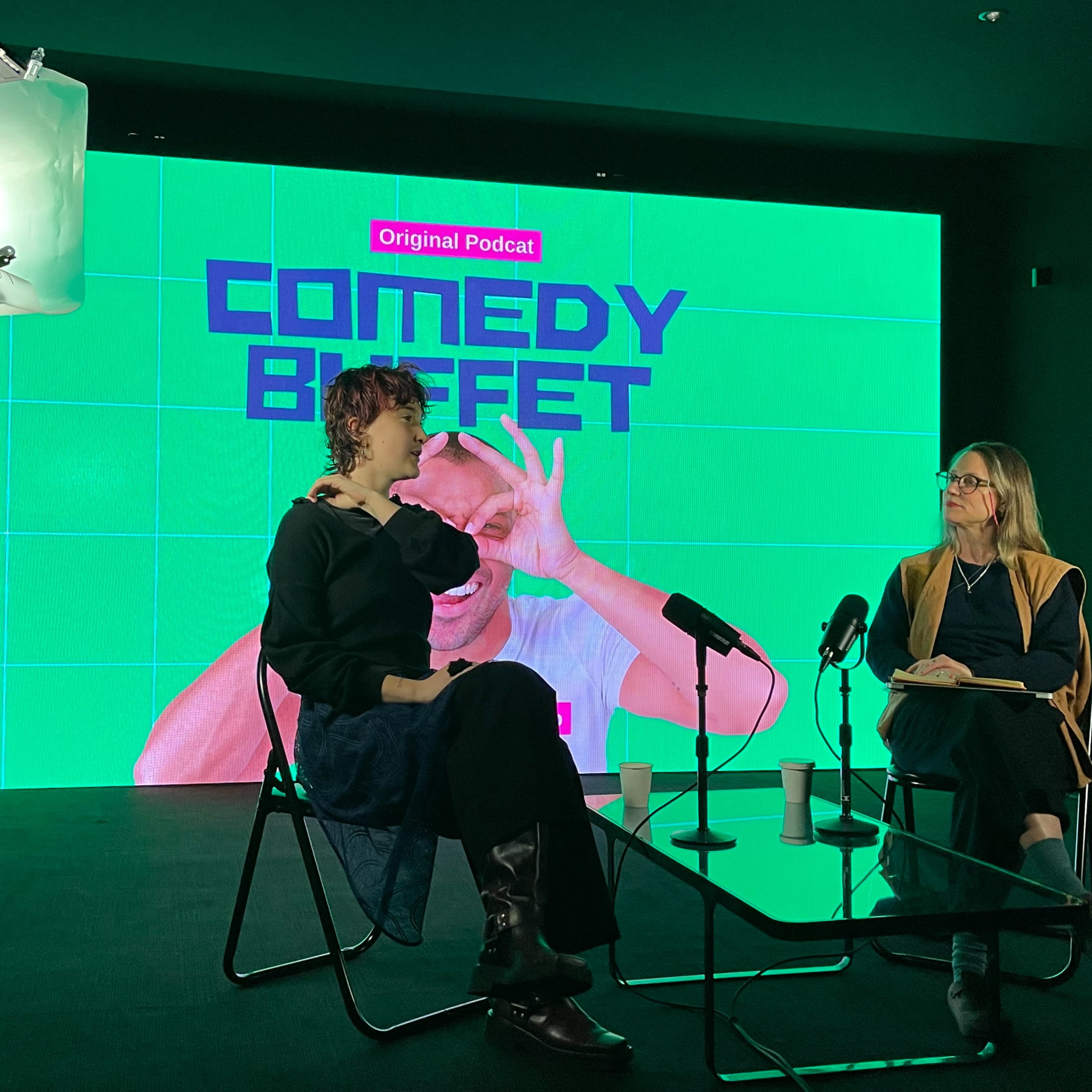 Two individuals are seated at a table discussing a podcast titled "Comedy Buffet," with a vibrant green backdrop displaying the podcast's logo.
