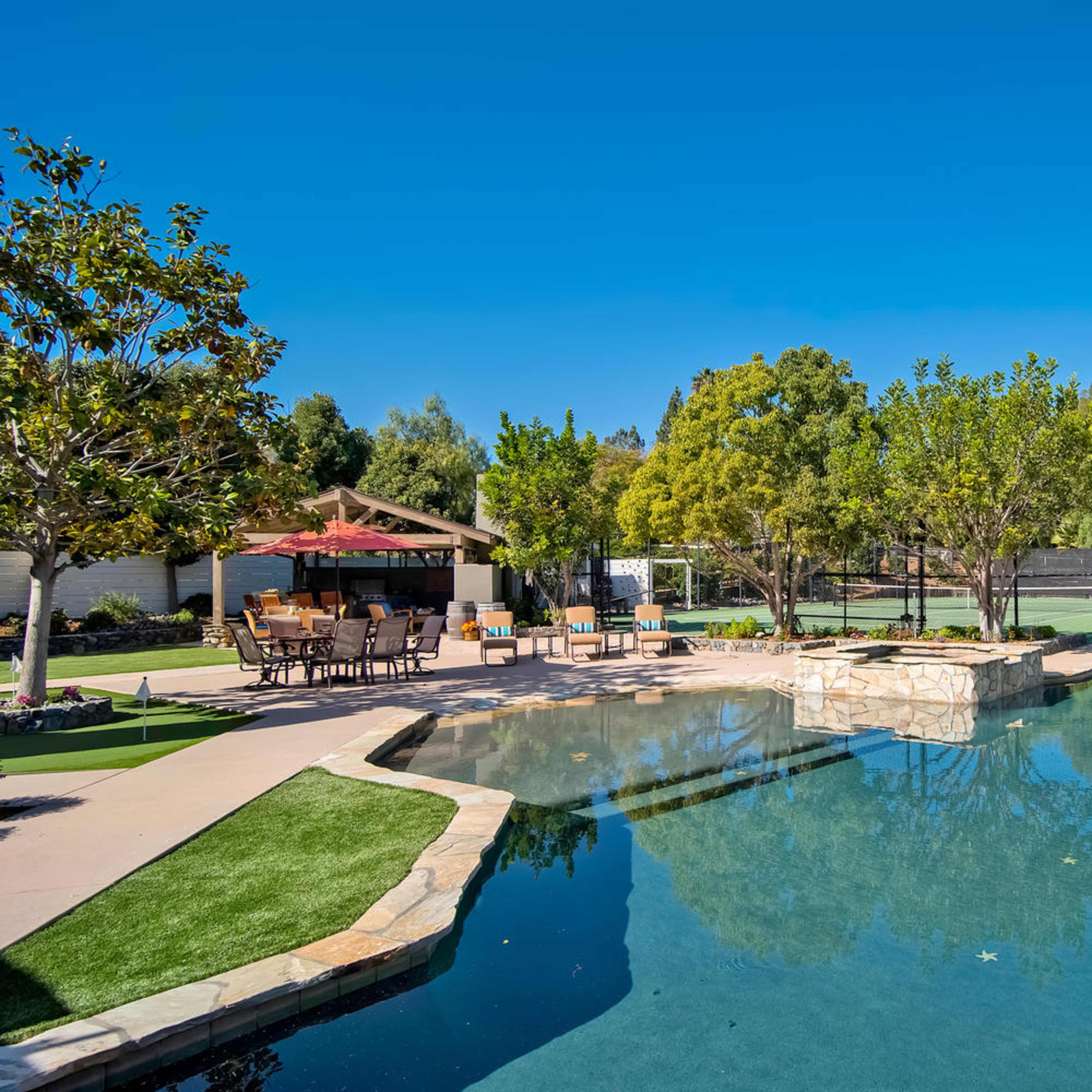 A swimming pool with stone accents, surrounded by landscaped greenery and outdoor seating areas.